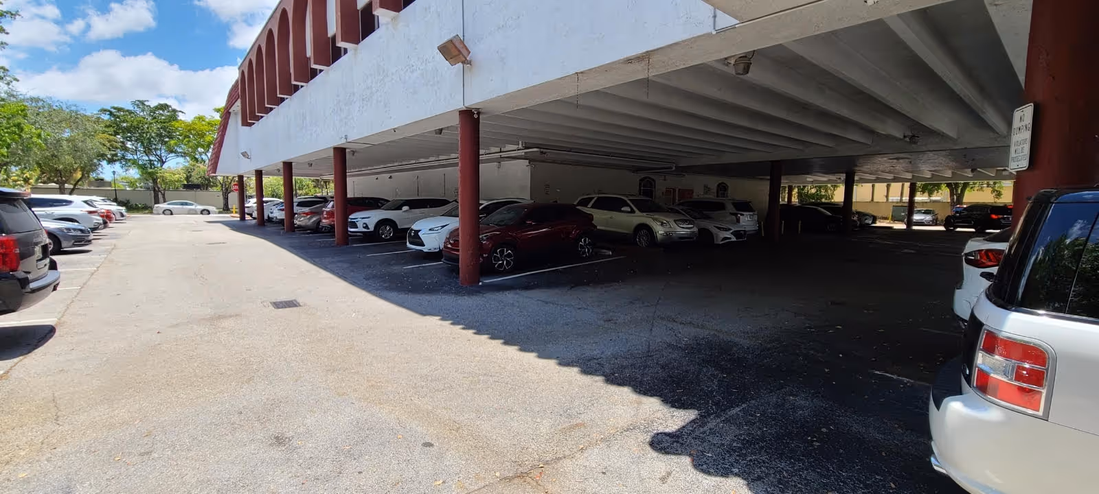 Covered parking area with numerous cars parked under a white and red building.