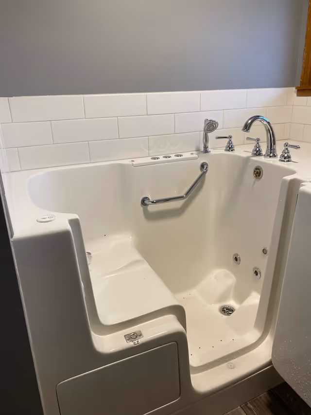 White accessible bathtub with built in seat and grab bar in a modern bathroom.