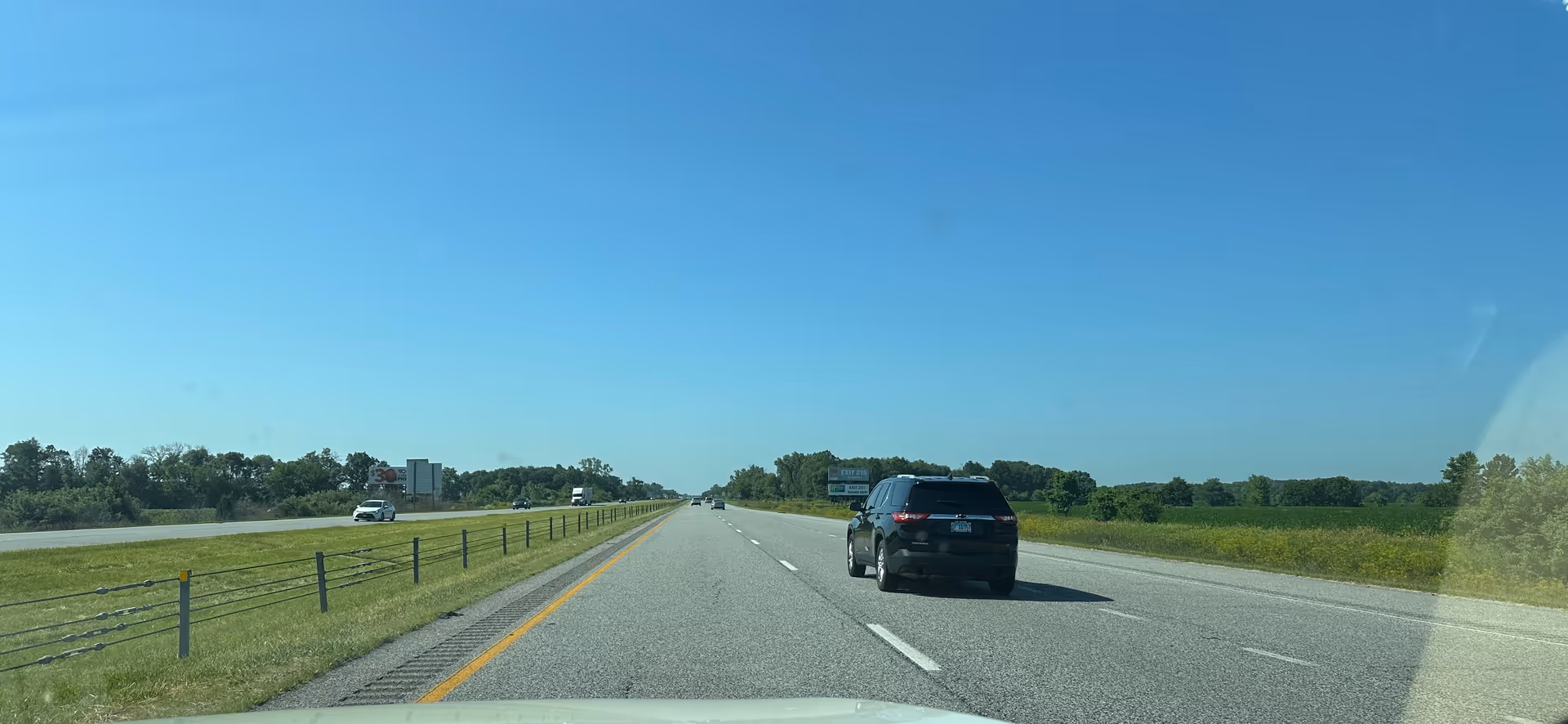 Road view from inside a vehicle shows highway, grassy median, and a black SUV ahead.