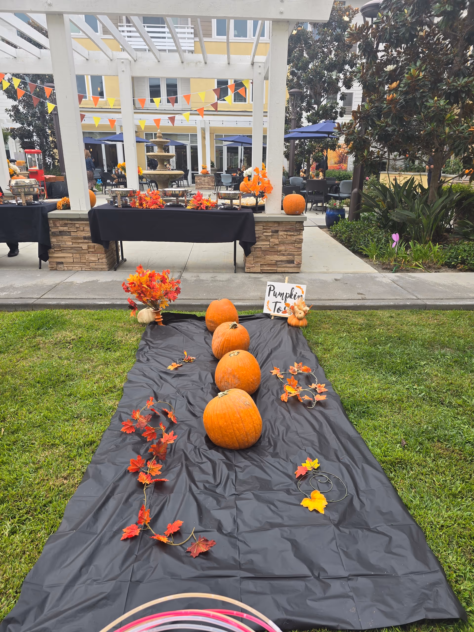 Outdoor courtyard with pumpkins, bunting, and a fountain under a white pergola.