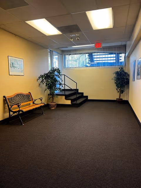 Interior hallway in a senior facility with a bench, plants, stairs, and an exit sign.