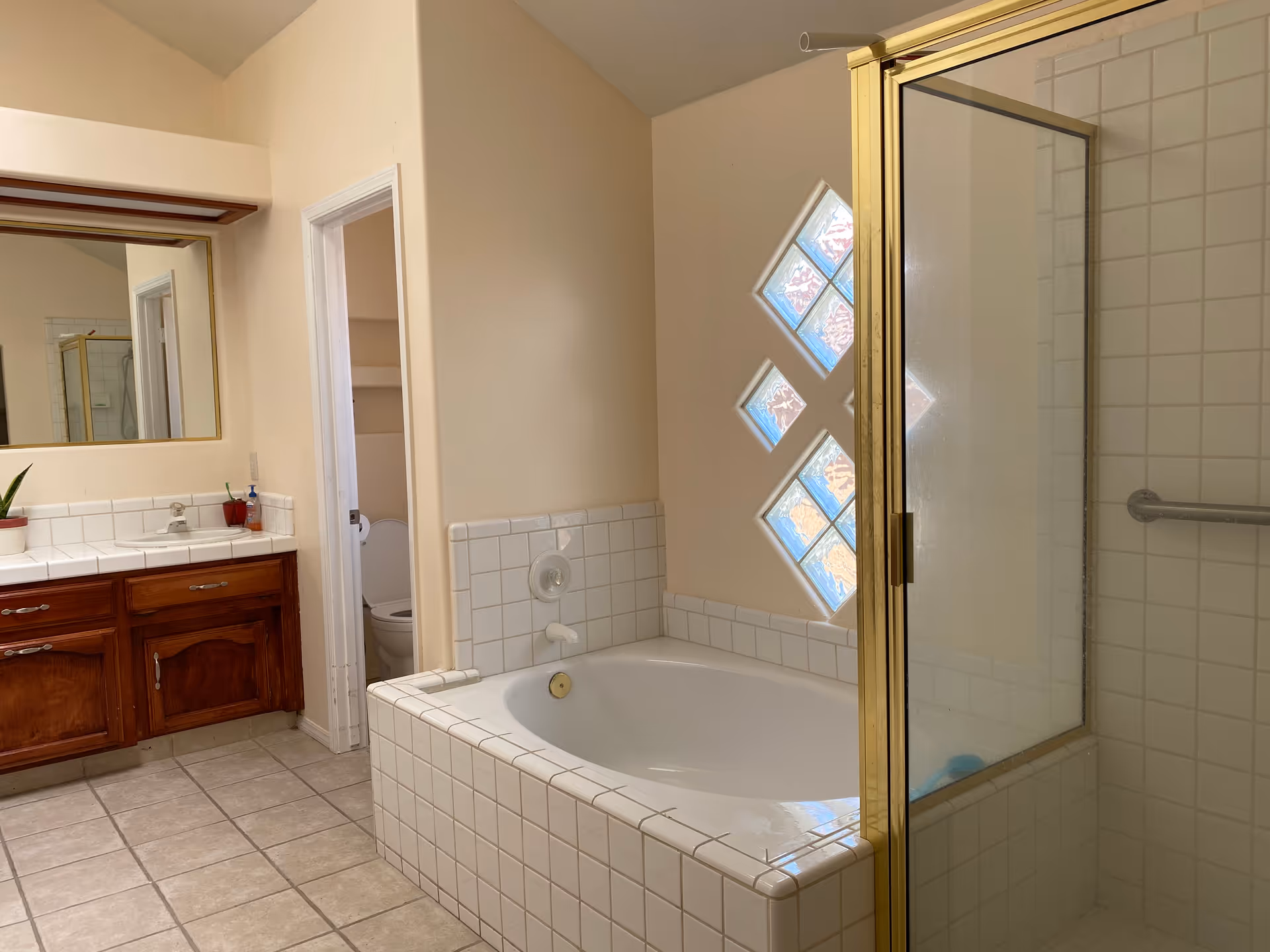 Bright bathroom with bathtub, glass shower, and wooden vanity under a mirror.
