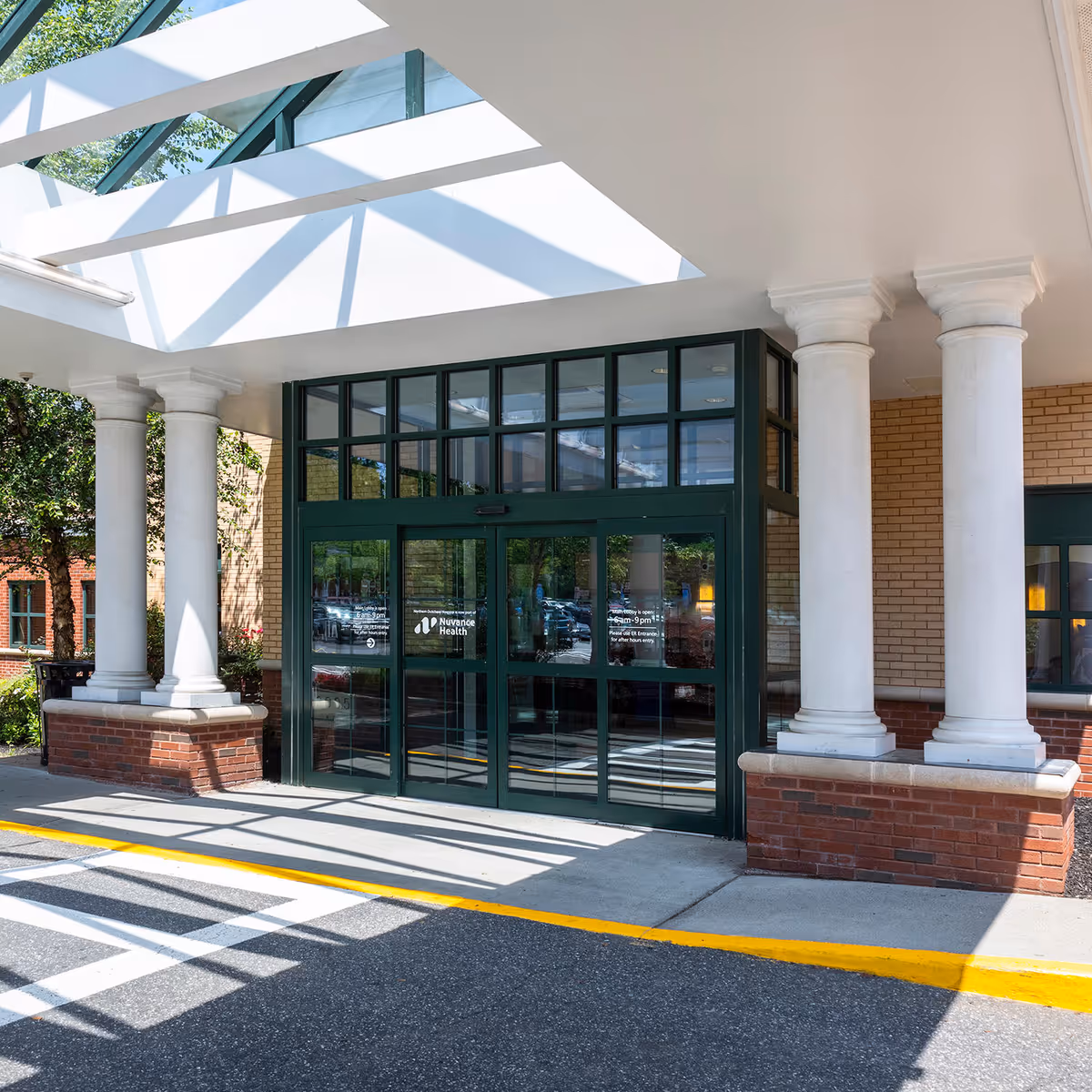 Entrance of a medical facility with glass doors, green frames, and white columns.