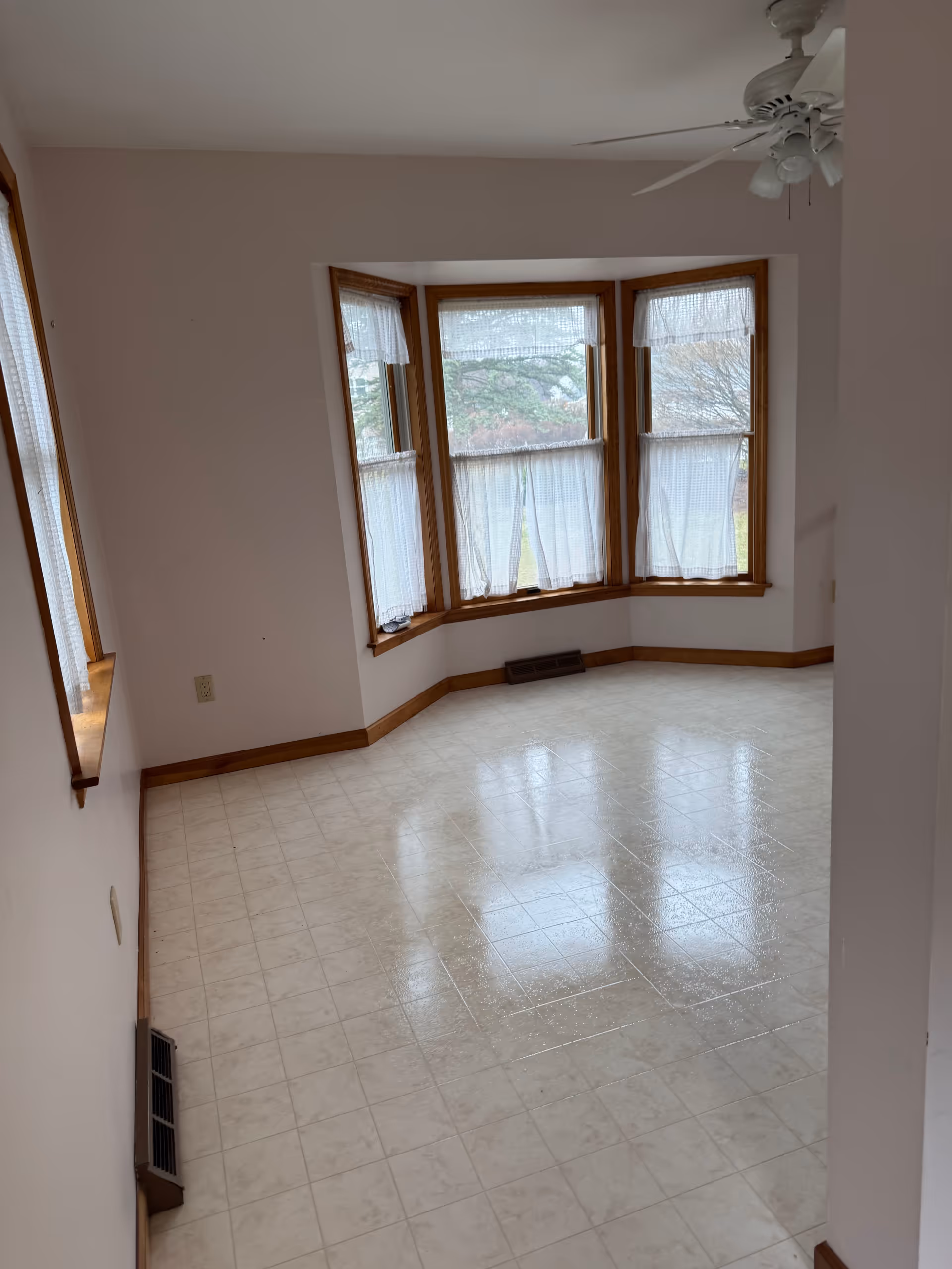 Bright, empty interior room with bay window, ceiling fan, and tiled floor.