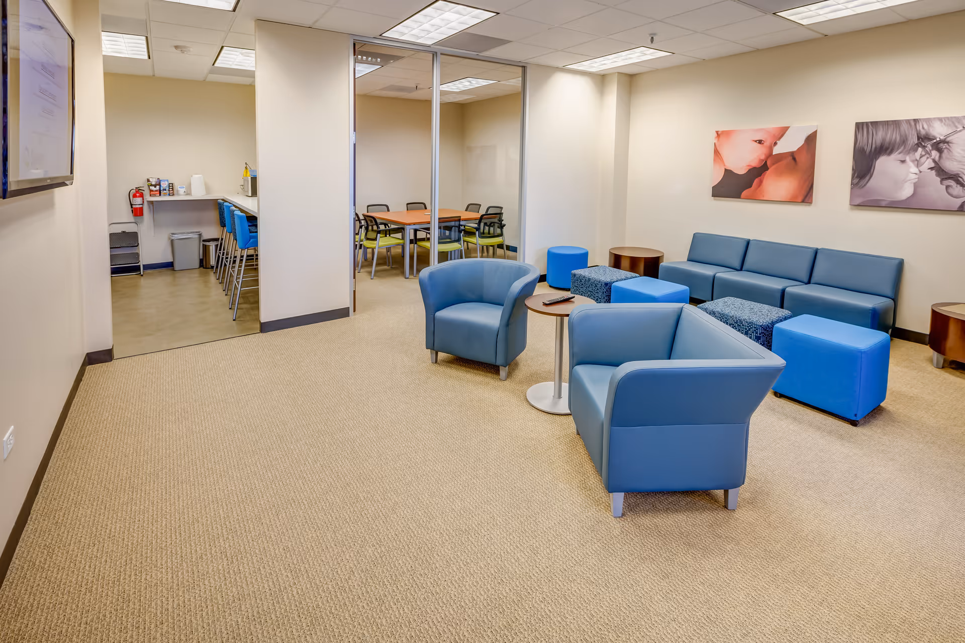 Bright modern lounge with blue seating and a kitchen area in the back.