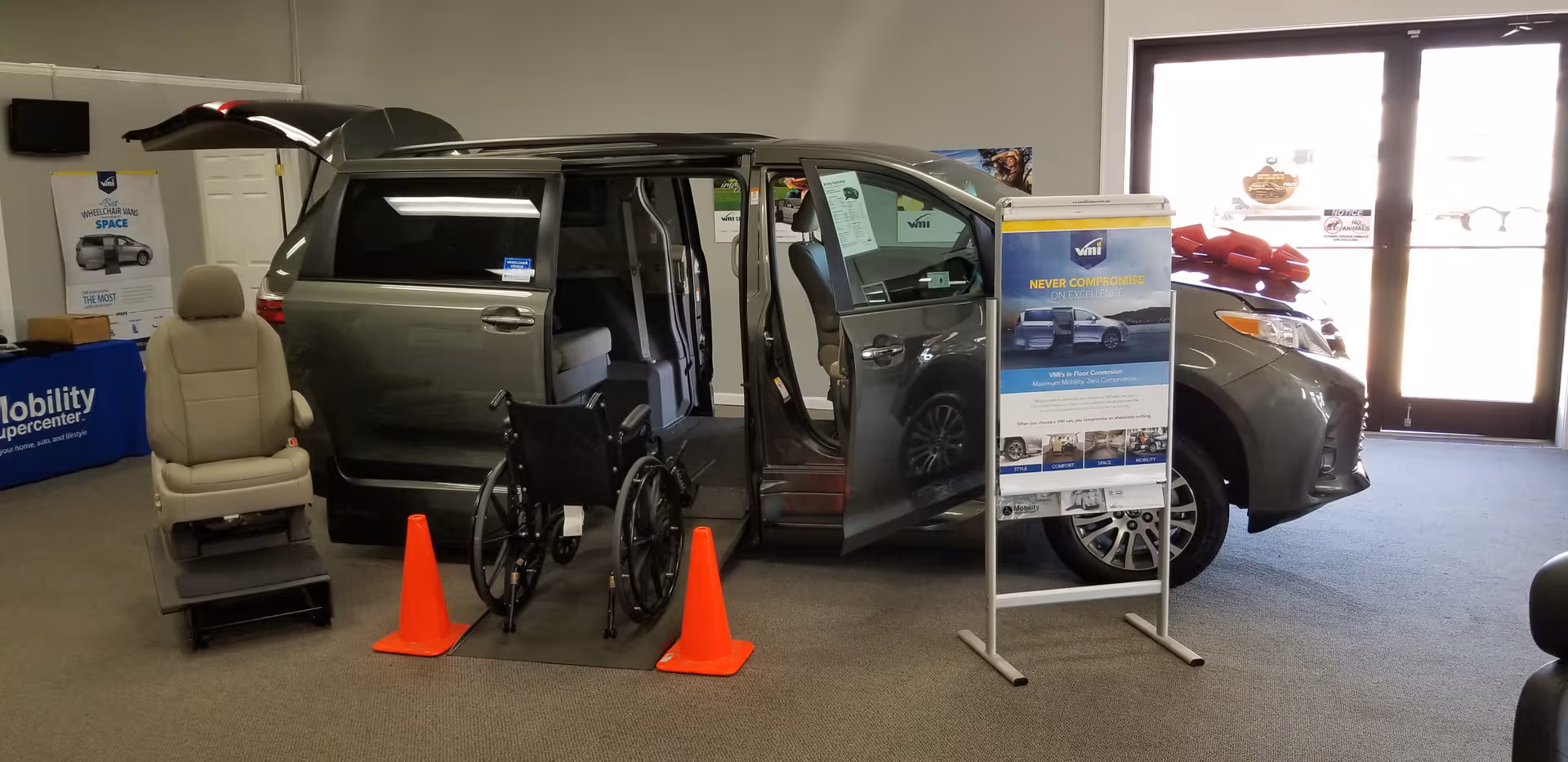 Inside MobilityWorks showroom, a wheelchair-accessible van with ramp is displayed beside a wheelchair and orange cones.