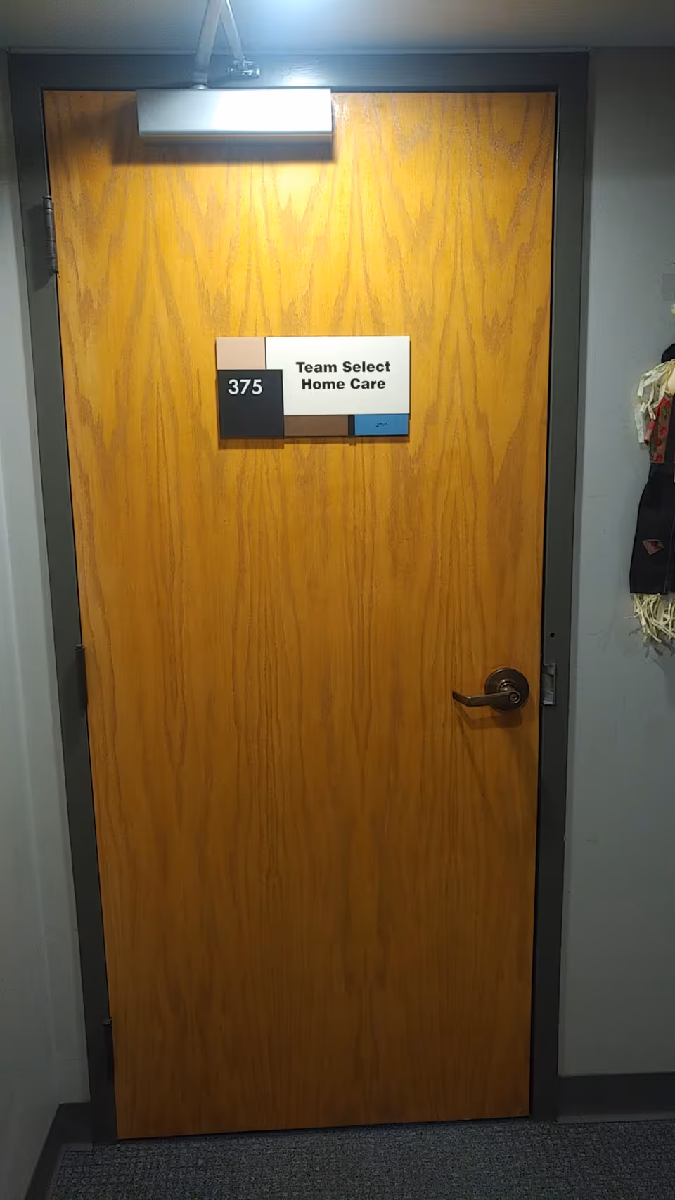 Wooden interior door with Team Select Home Care sign and room number 375.