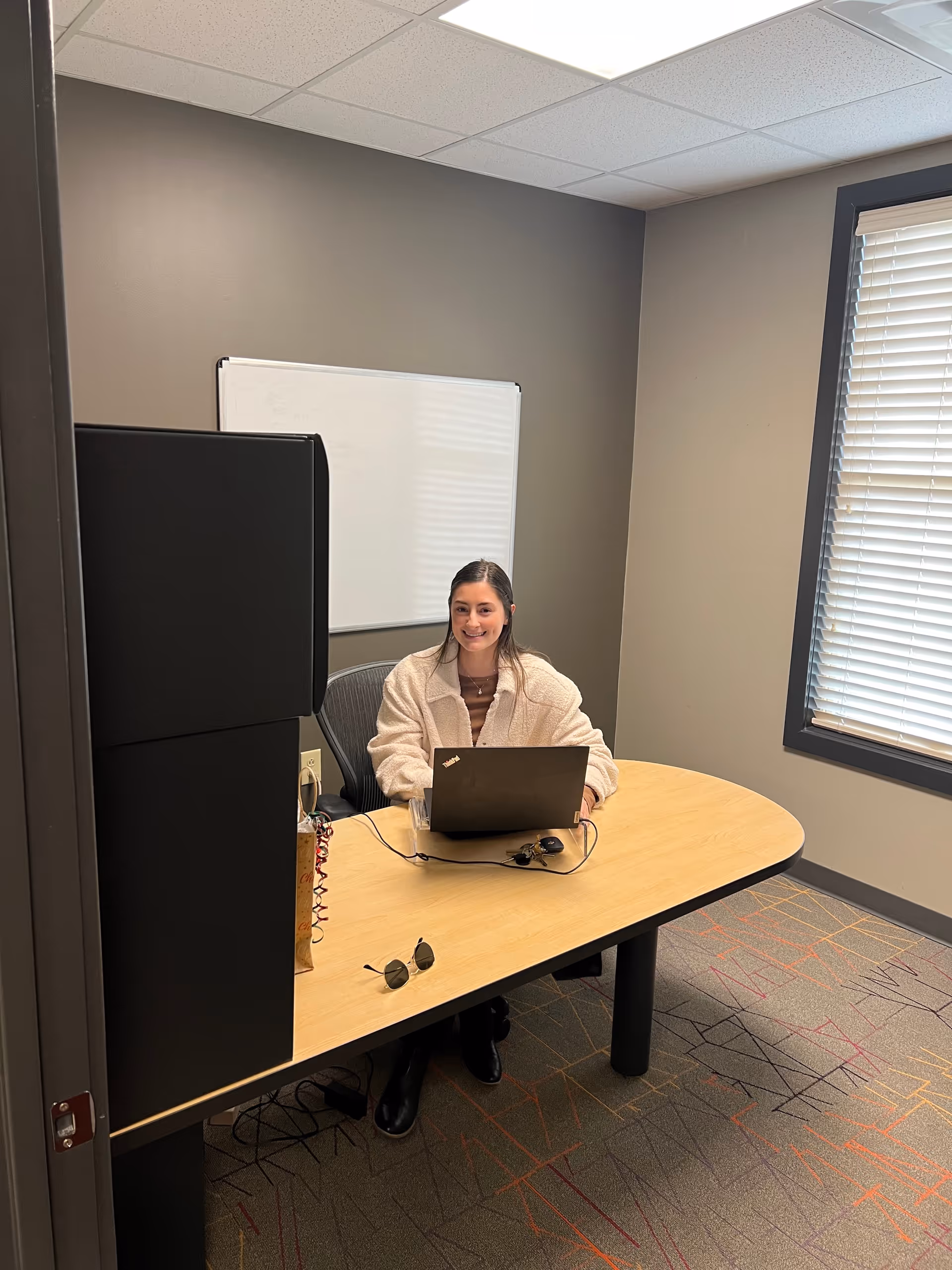 A person sits at a wooden desk in a small office with a laptop.