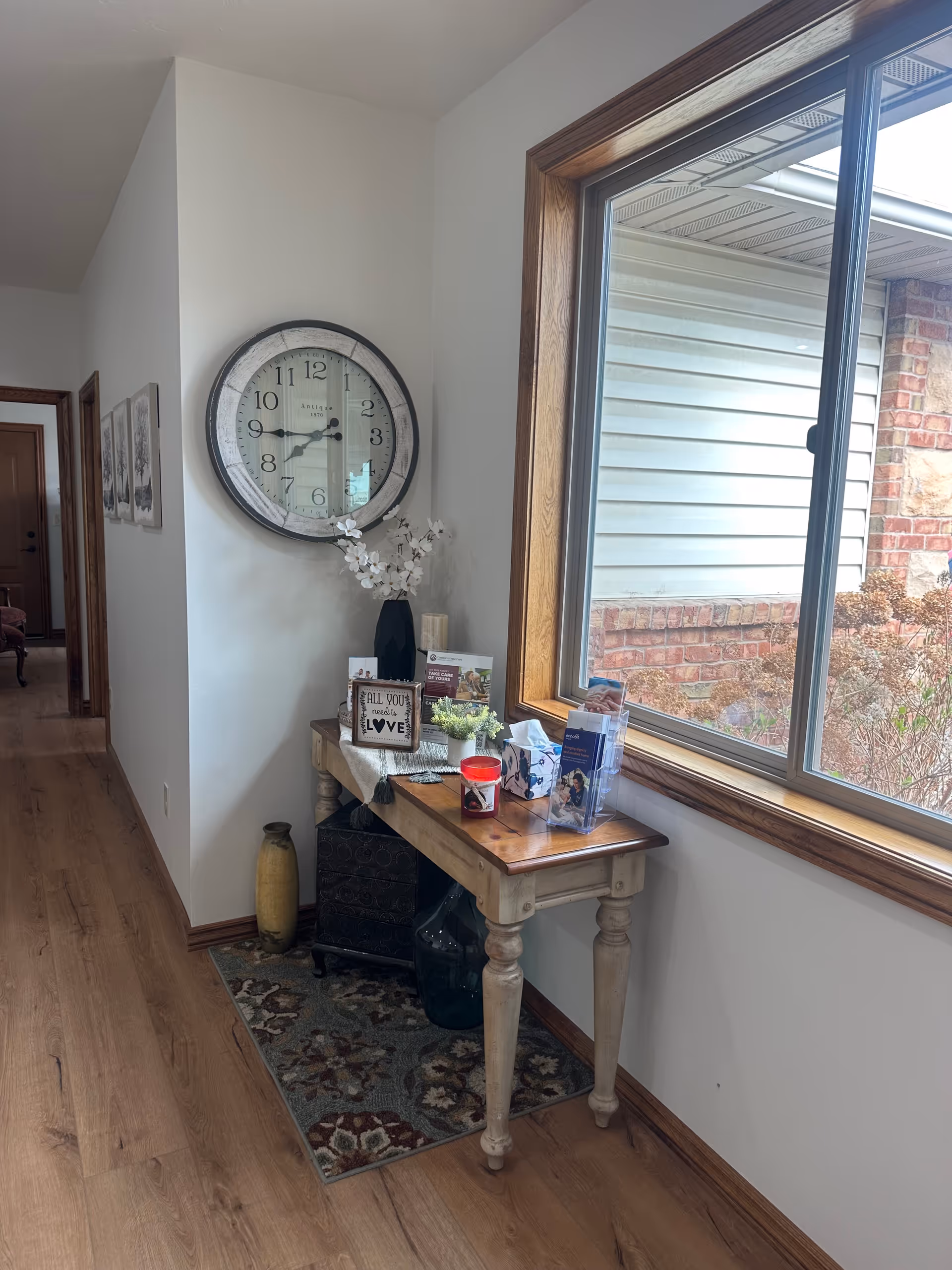 Hallway alcove with a wooden console table, large clock, and window view.