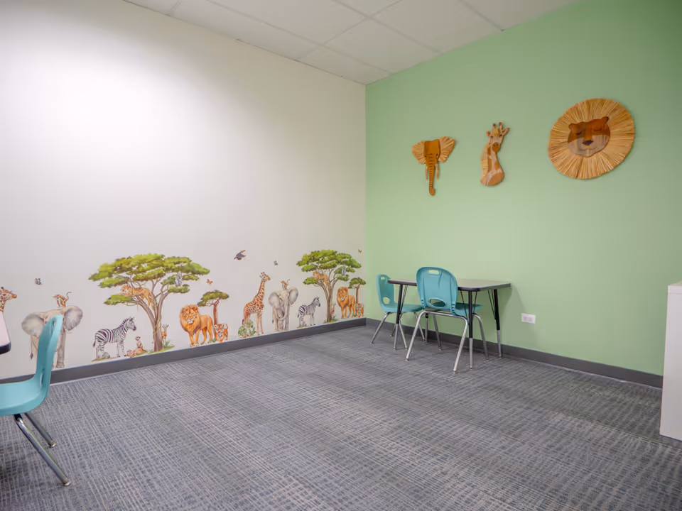 Interior room with a green wall, animal mural, and turquoise chairs around a small table.
