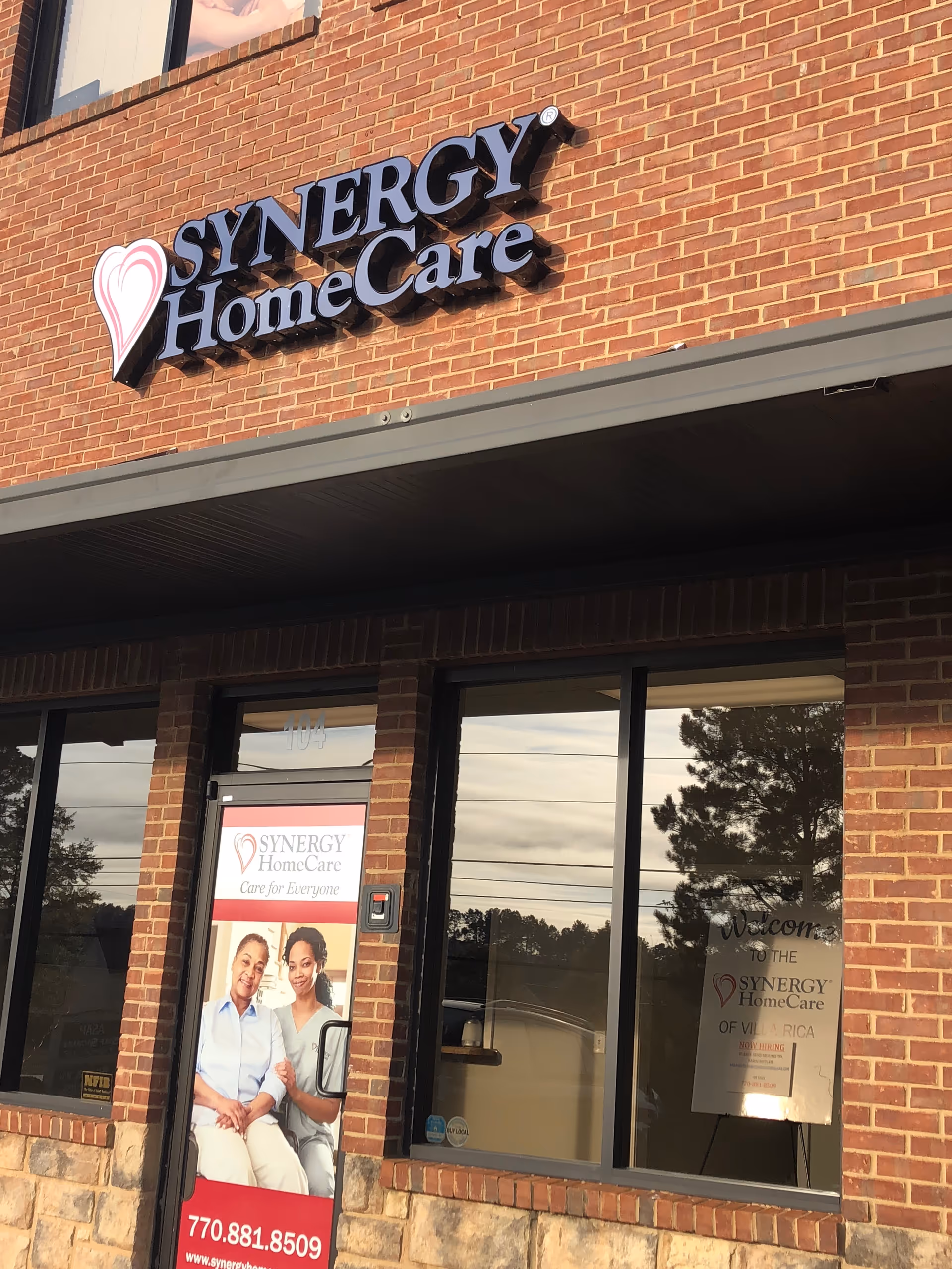 Brick building exterior with SYNERGY HomeCare sign and large storefront windows.