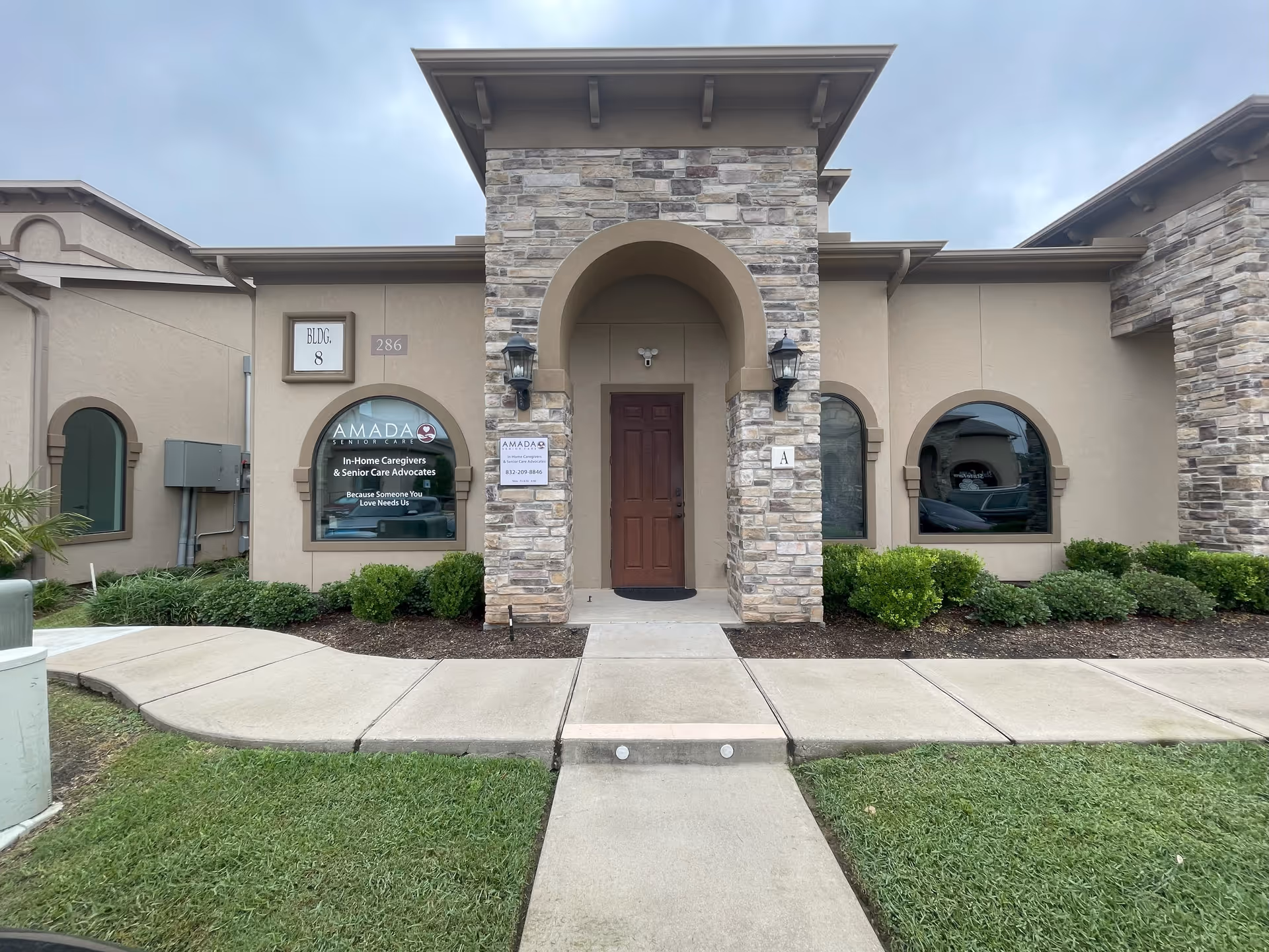 Front entrance of Amada Senior Care facility with stone archway and arched windows.
