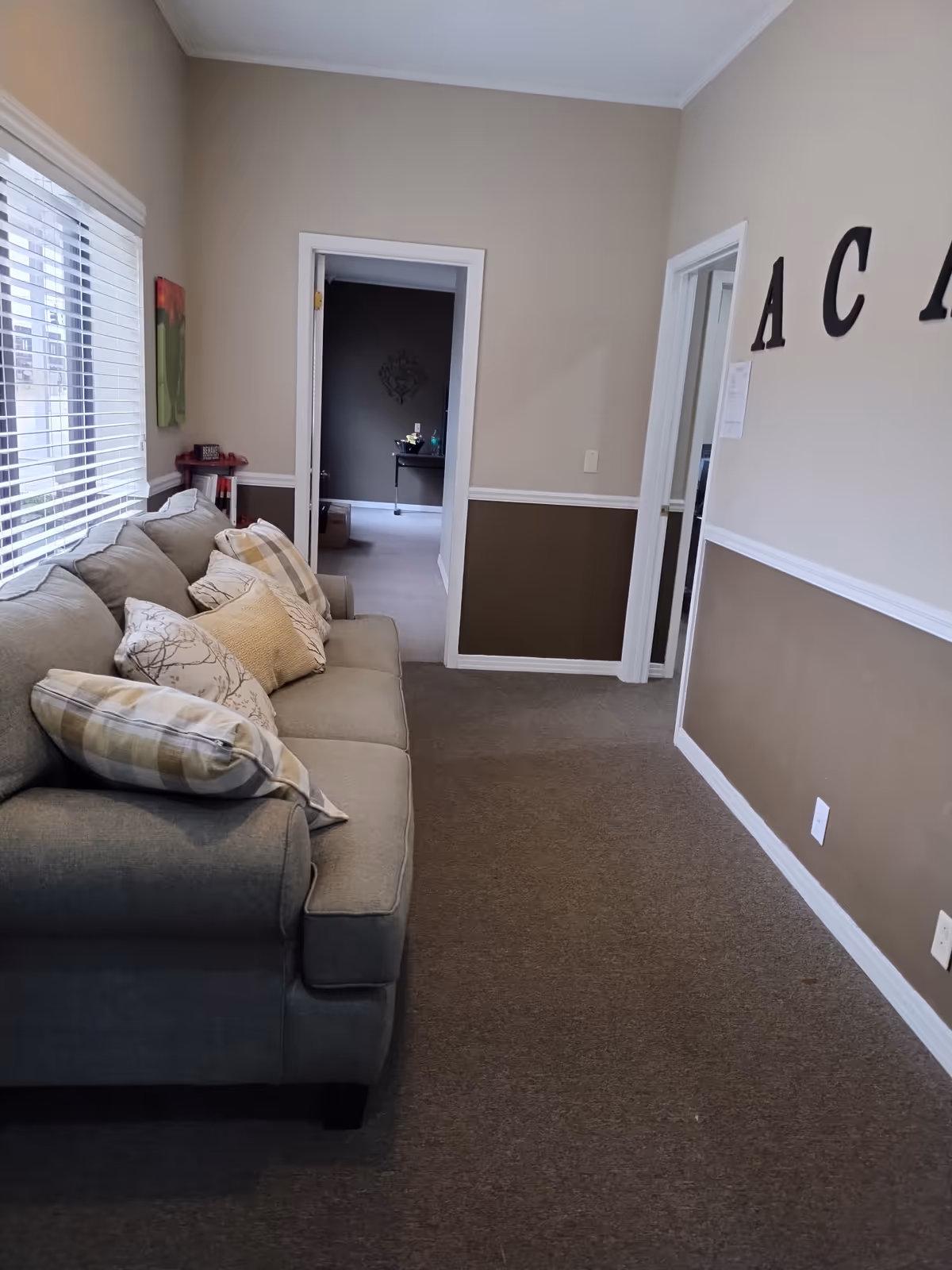 Grey sectional sofa in a beige-walled living area with windows.