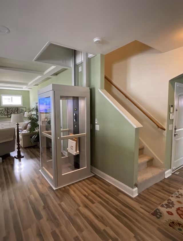 Interior of a senior living facility featuring a modern residential elevator beside a stairway.
