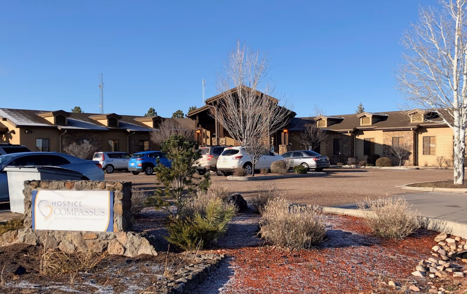 Exterior view of a Compassus hospice facility with a parking lot and landscaped entrance.
