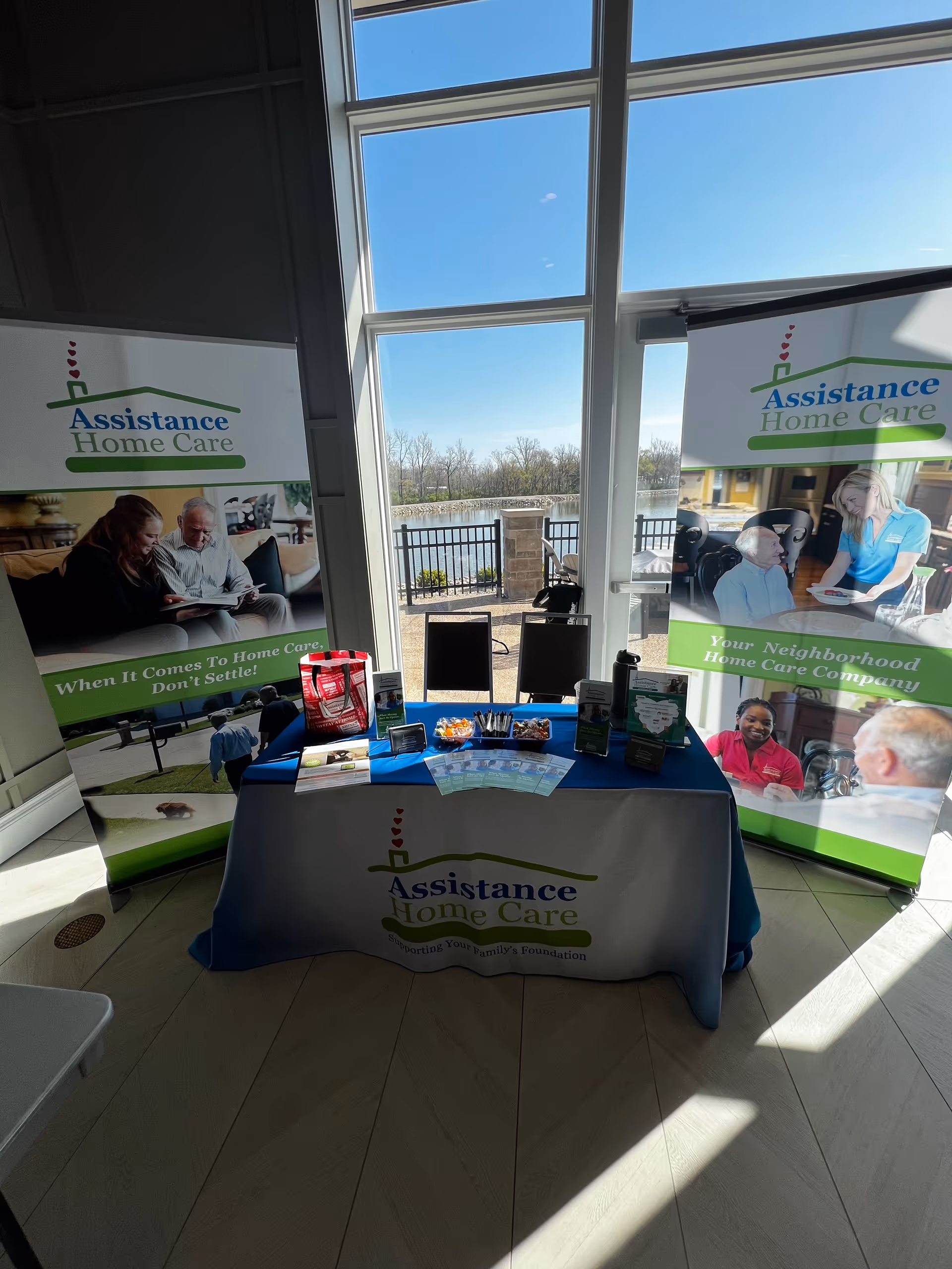 Indoor booth setup with banners, a table, and brochures for Assistance Home Care.