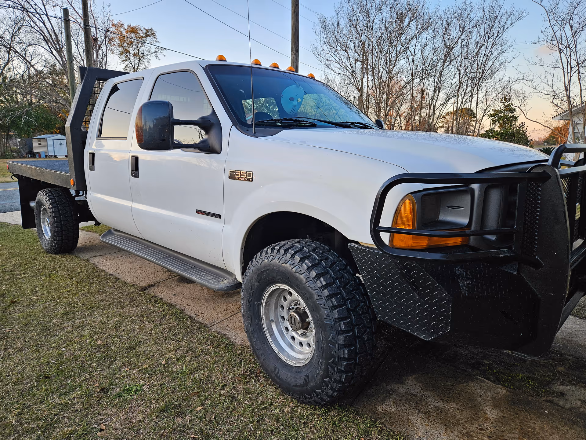 White heavy-duty pickup truck parked on a lawn with a metal flatbed and bumper guard