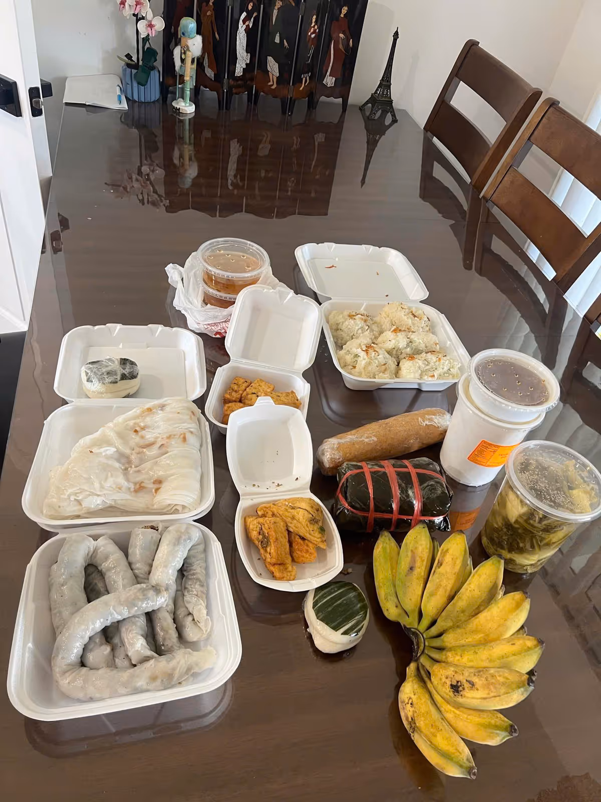 Takeout meals and bananas laid out on a glossy dining table in a residential dining room.