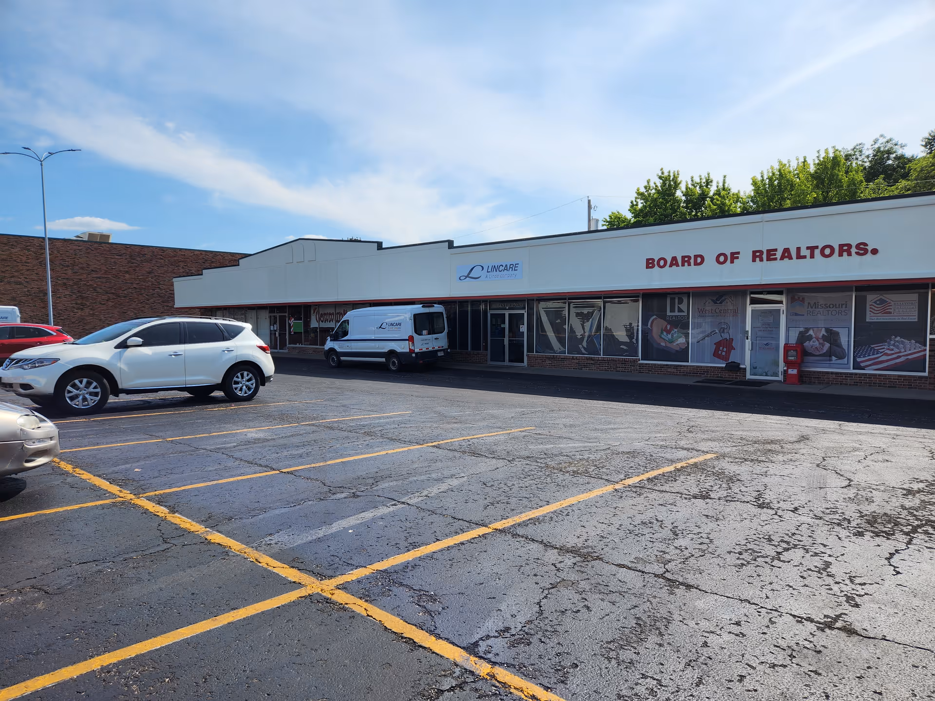 Exterior view of a strip mall with Lincare sign and Realtors signage, parking lot in front.