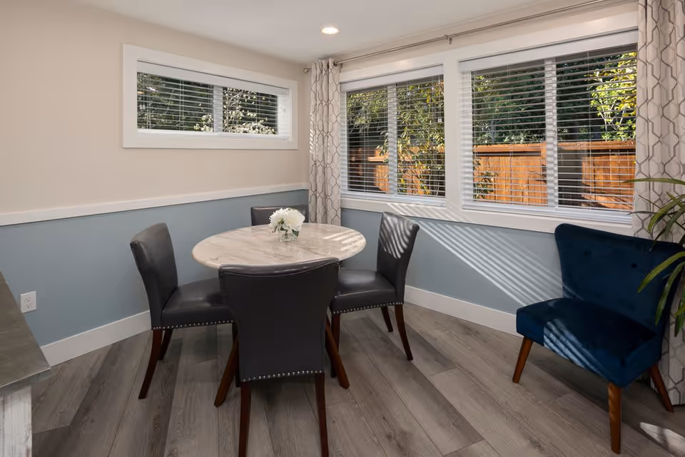 Light-filled dining area with round marble table and four upholstered chairs.