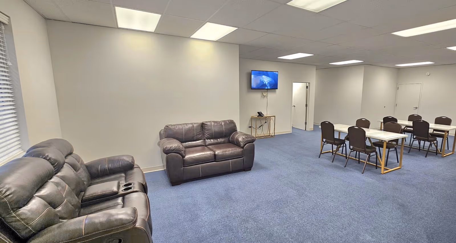 A spacious senior living common area with leather seating, a TV, and dining tables.