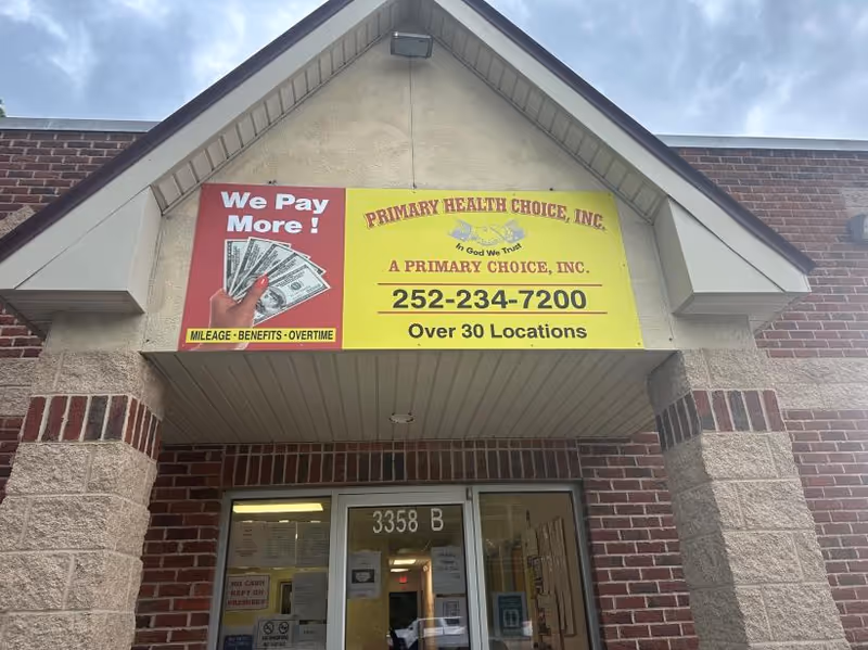Brick building entrance with a large yellow sign for Primary Health Choice and services.