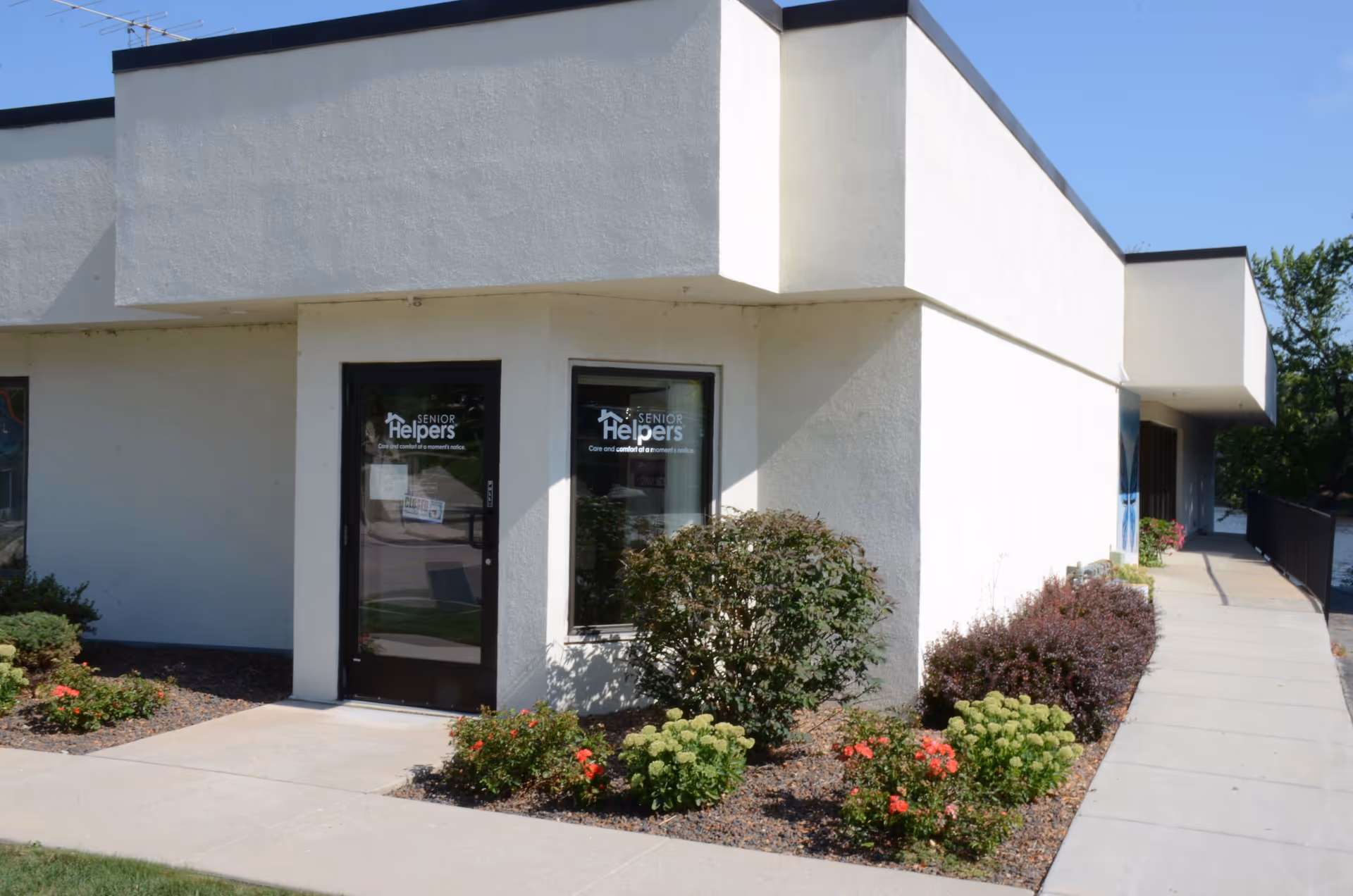 White, modern senior care building exterior with a glass entrance and landscaped front yard.