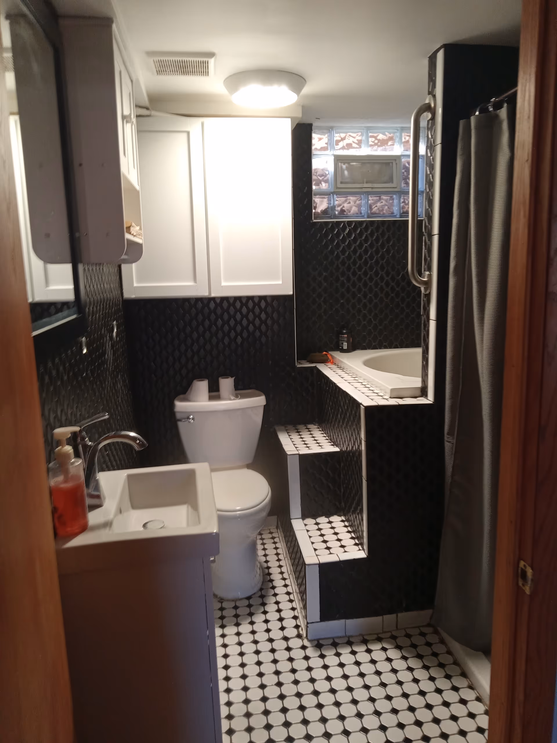 Compact bathroom in a senior living facility featuring white sink, toilet, and shower with black tile.