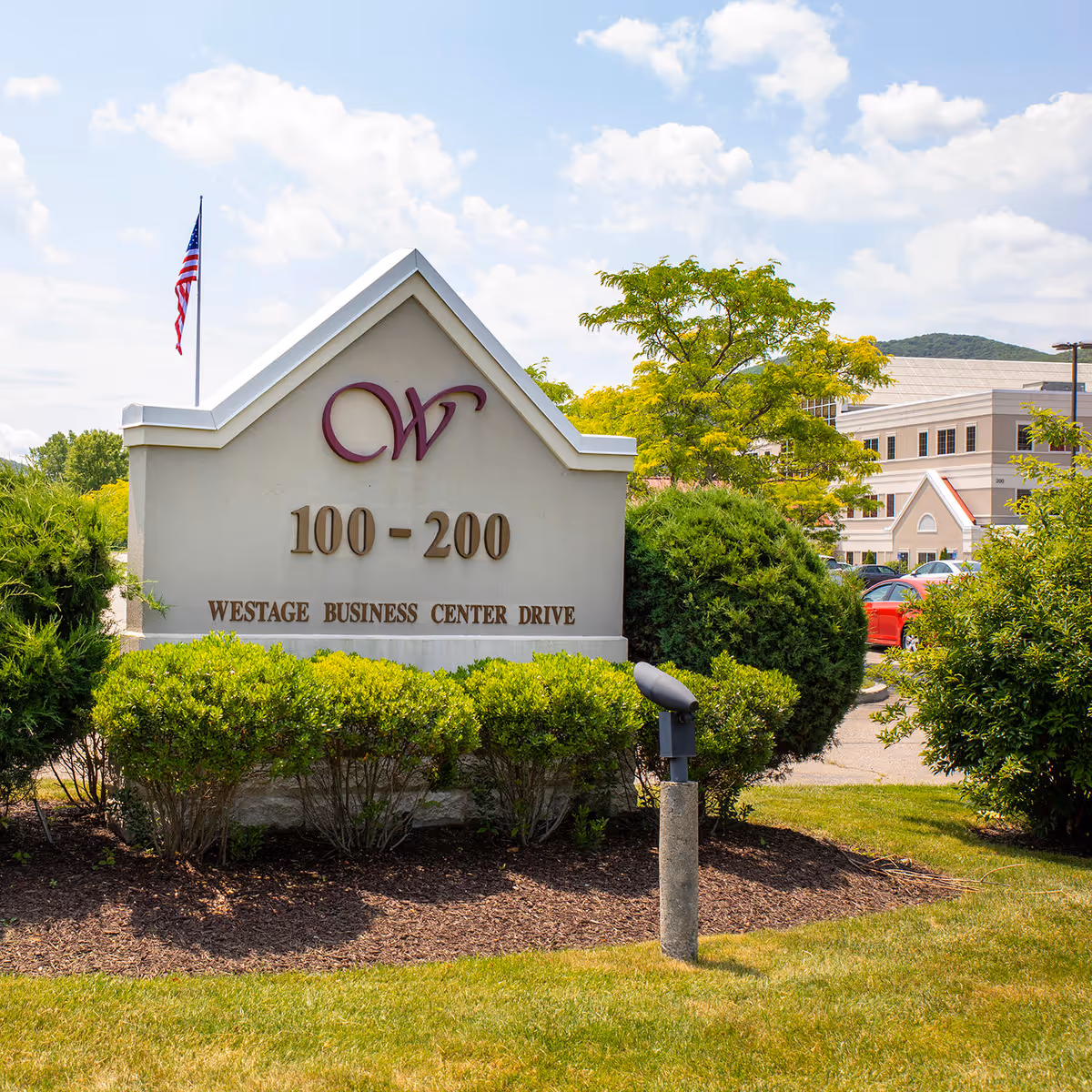 Stone sign with CW logo and 100-200 Westage Business Center Drive surrounded by shrubs
