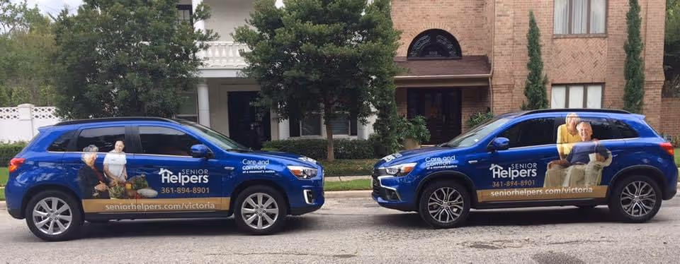 Two blue Senior Helpers vans parked along a street in front of a brick building.