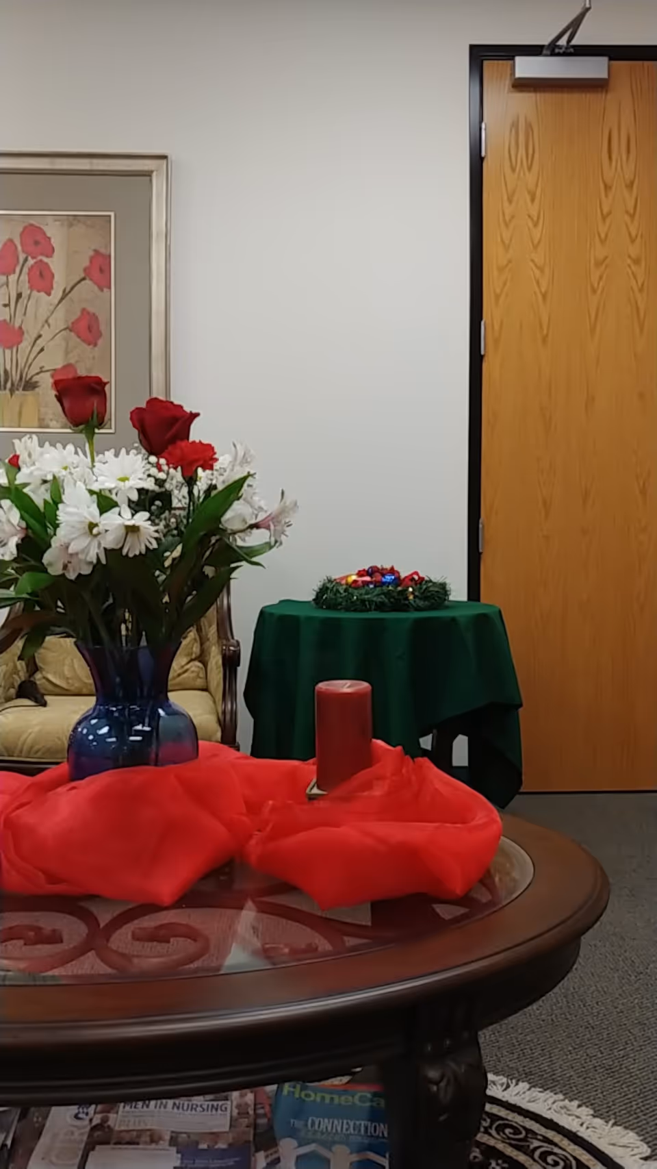 Round wooden coffee table with red candle, flowers, and cloth in a living room.
