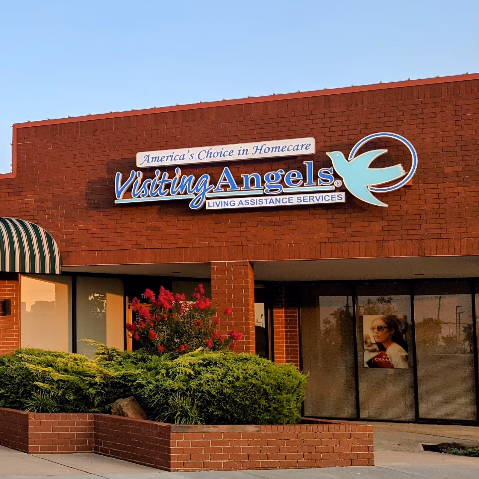 Exterior brick building with Visiting Angels sign and landscaped shrubs in front.