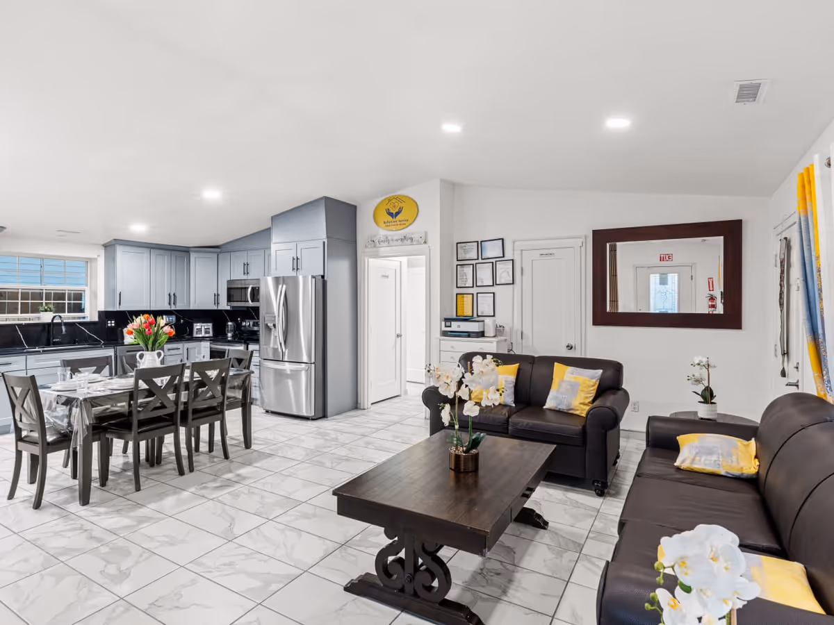 Open, well-lit living area with dark sofas and a modern kitchen.