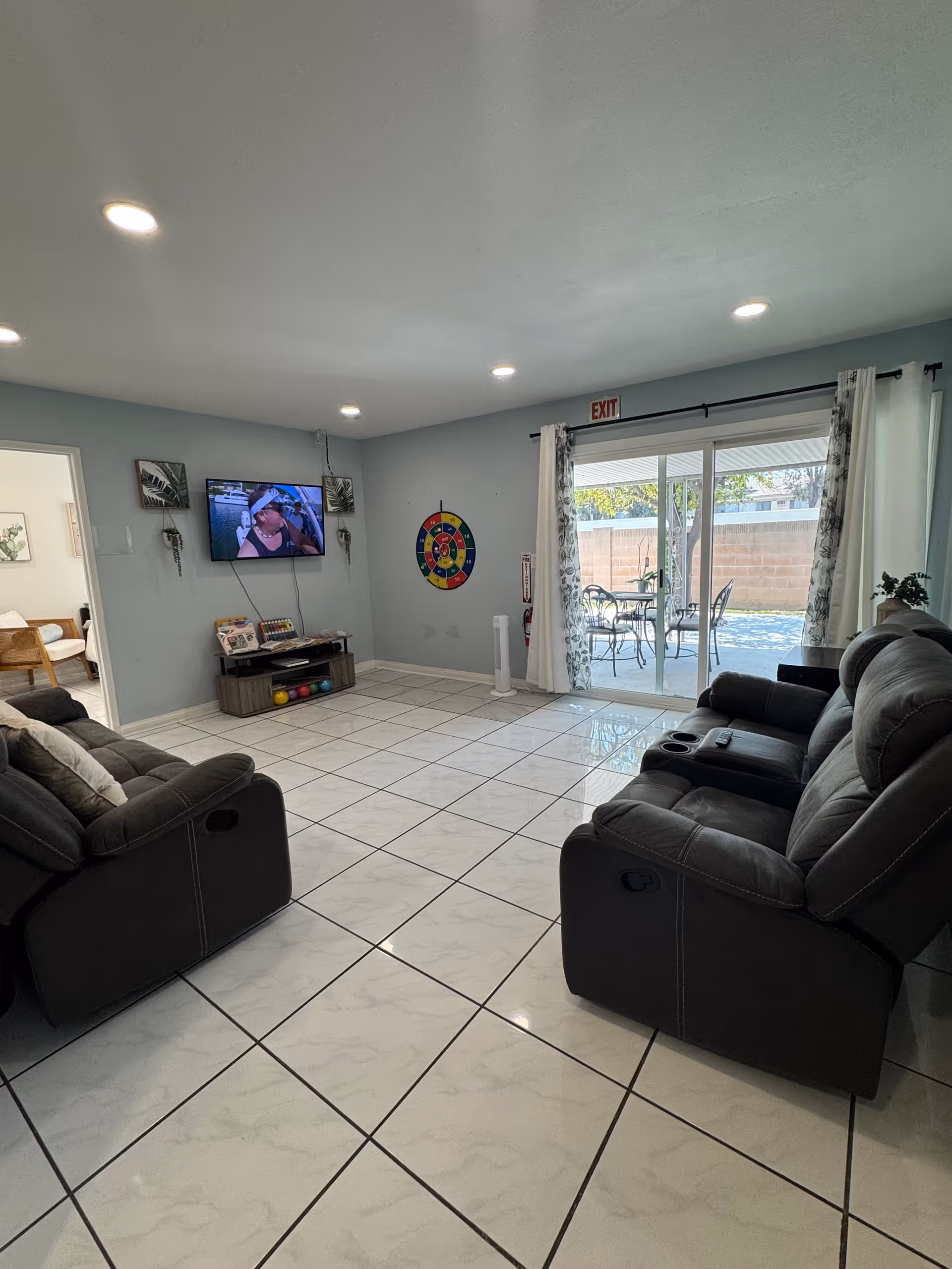 A spacious living room with dark recliners, TV, and sliding patio doors.