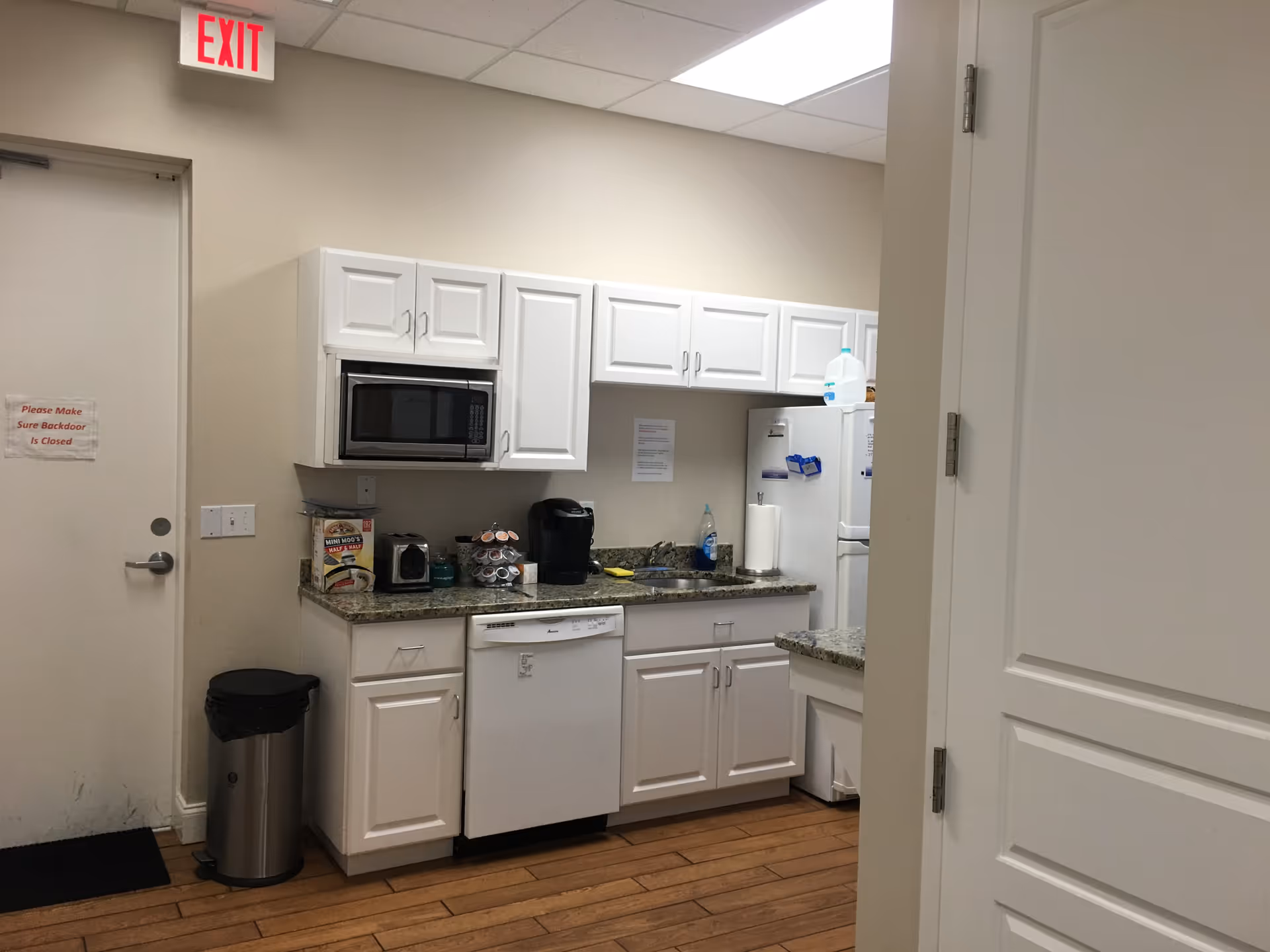Compact kitchen area with white cabinets, appliances, and a microwave in a senior living facility.