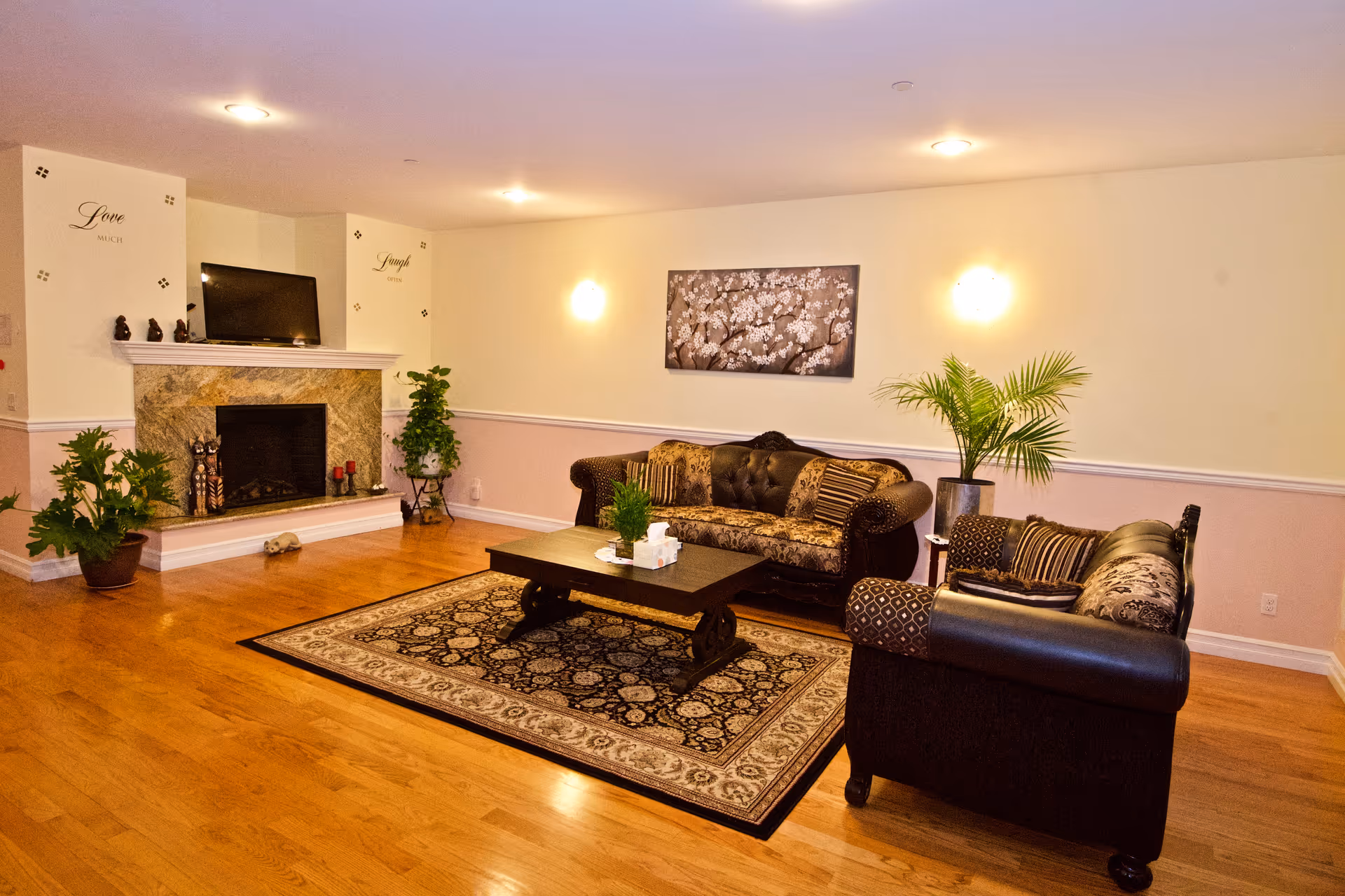 Cozy senior living lounge with fireplace, couches, plants, and a coffee table.