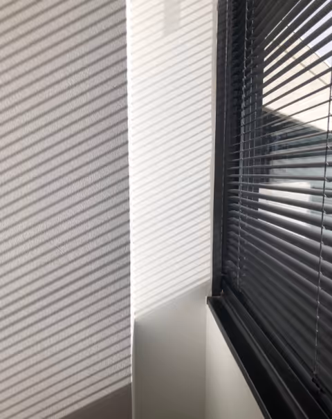 Interior corner with window blinds casting striped shadows on the wall.