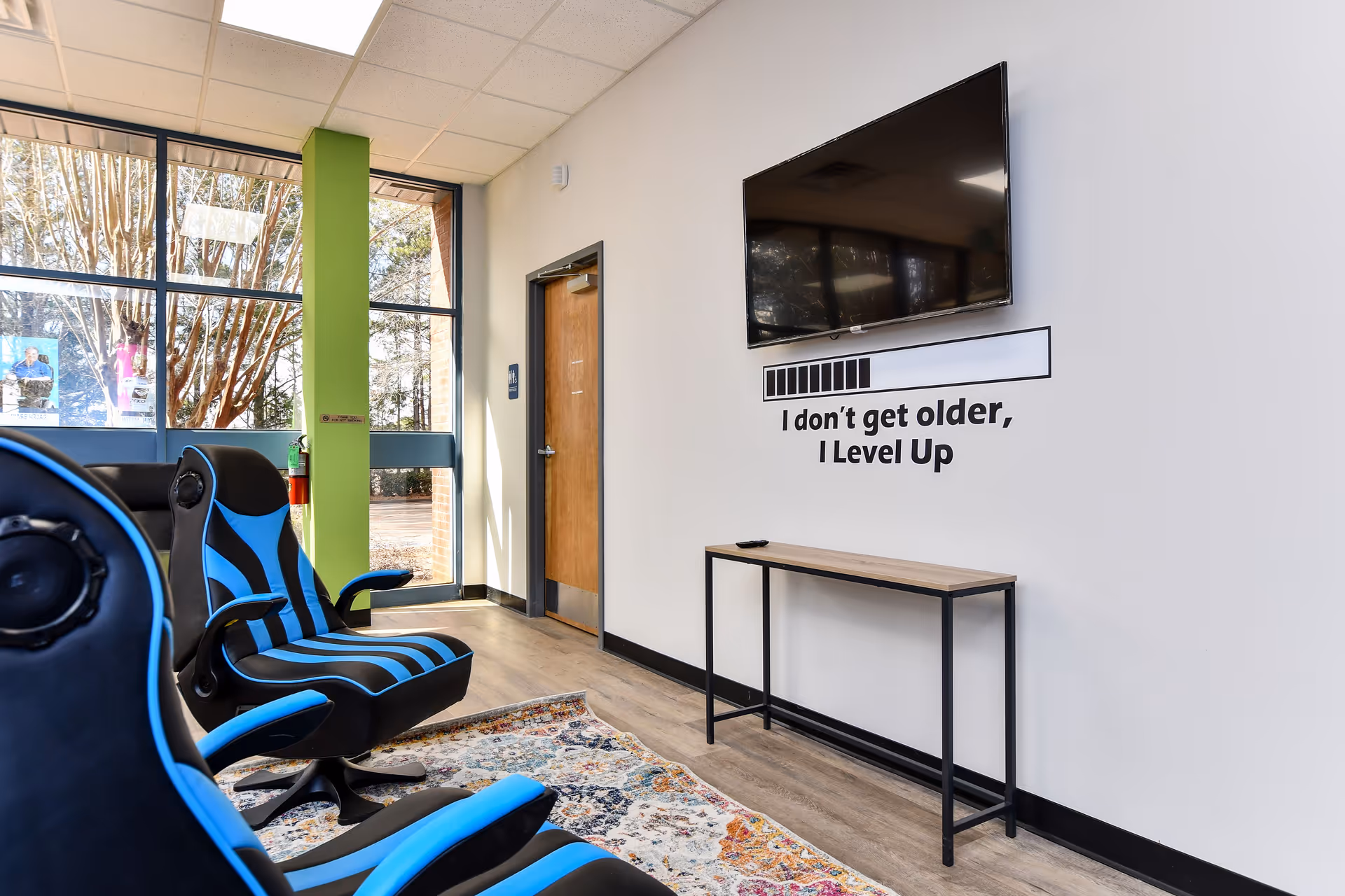 Interior lounge with blue gaming chairs, wall-mounted TV, and a motivational quote.