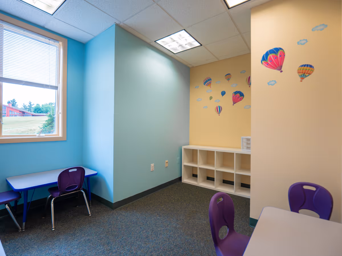 Bright, colorful interior play area with cubby shelves, small tables, and purple chairs.