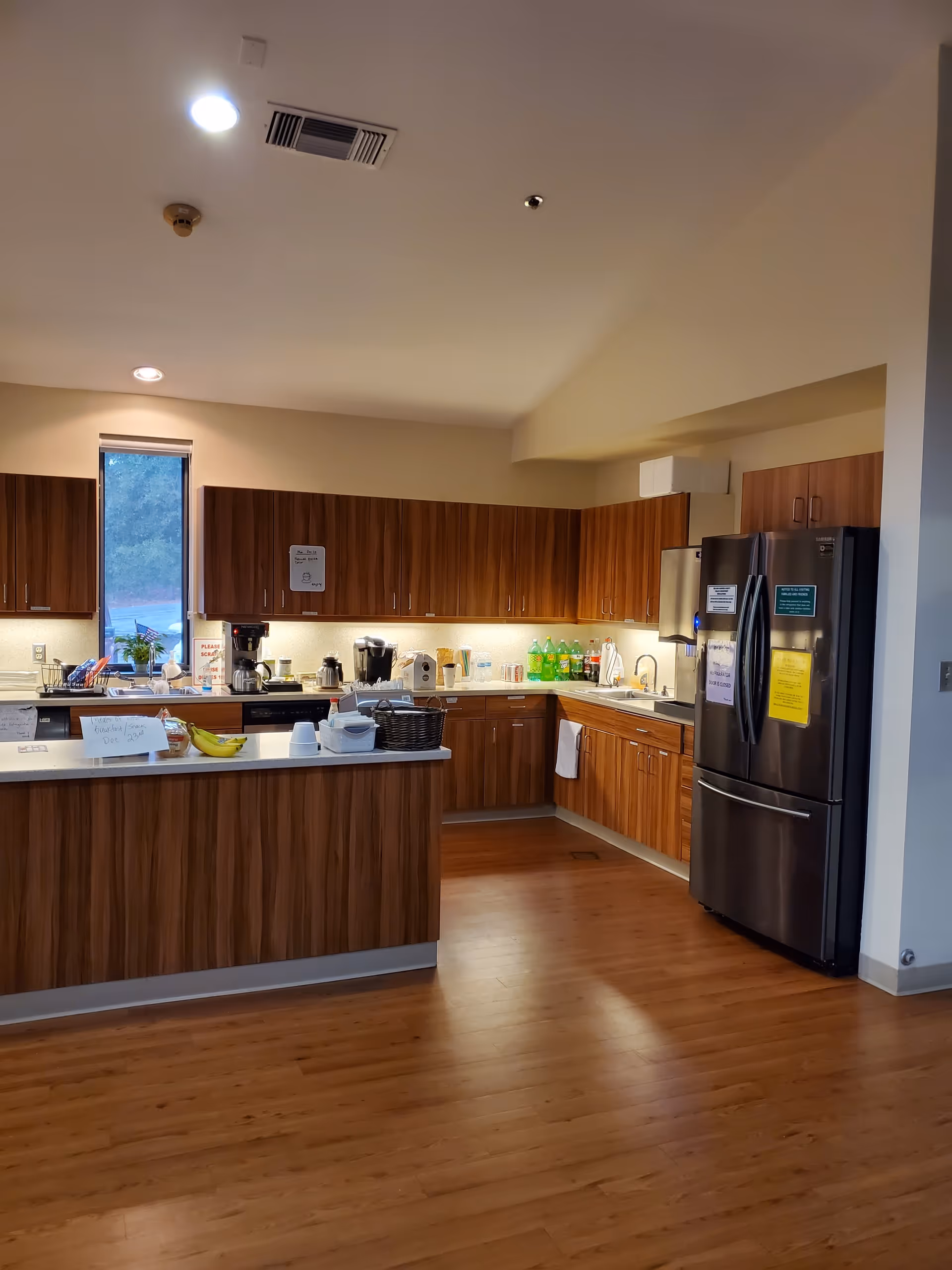 Well-lit wood-finished kitchen with counters, appliances, and a stainless refrigerator.