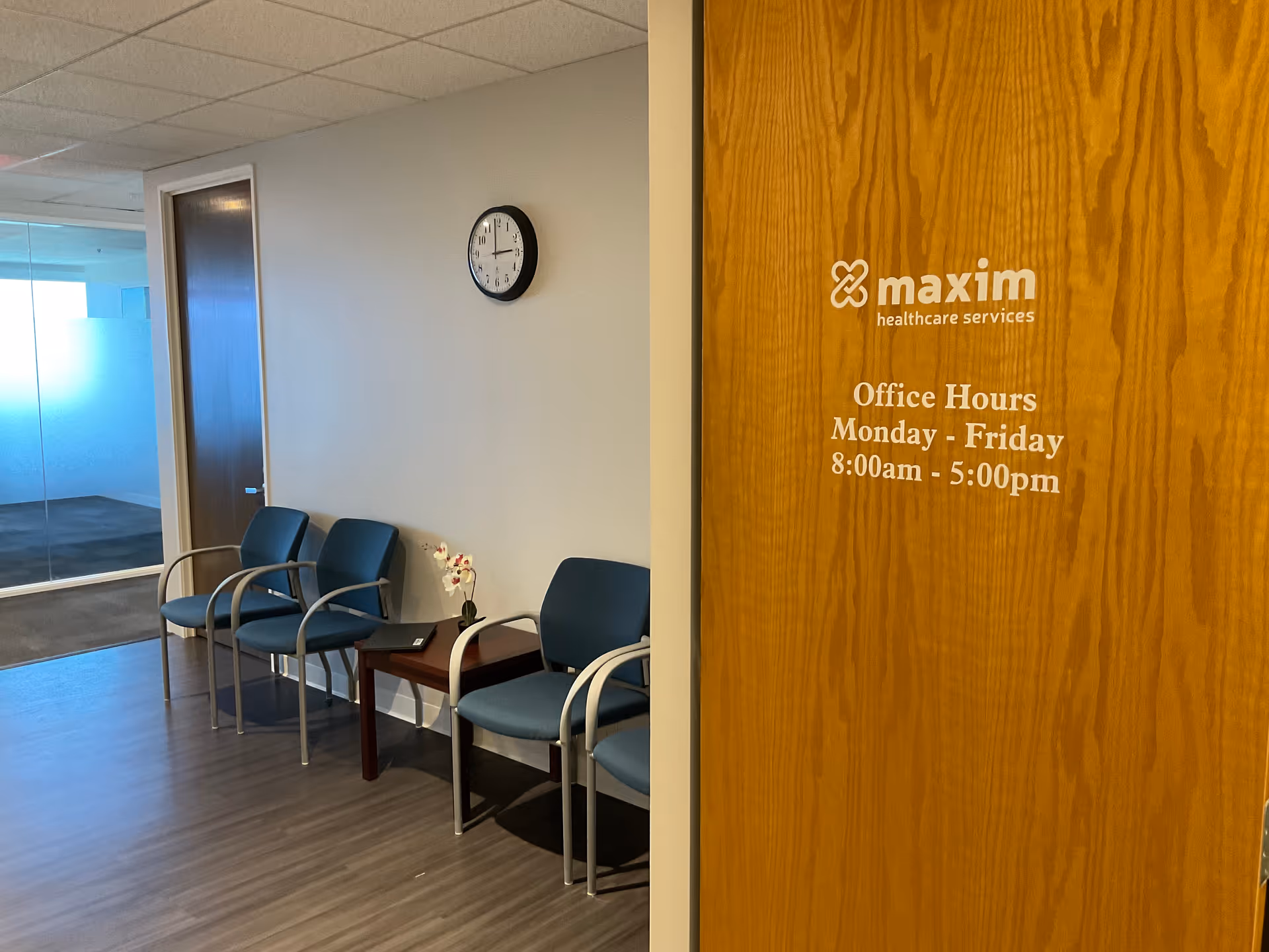 Interior waiting area with blue chairs, clock, and a door displaying office hours.