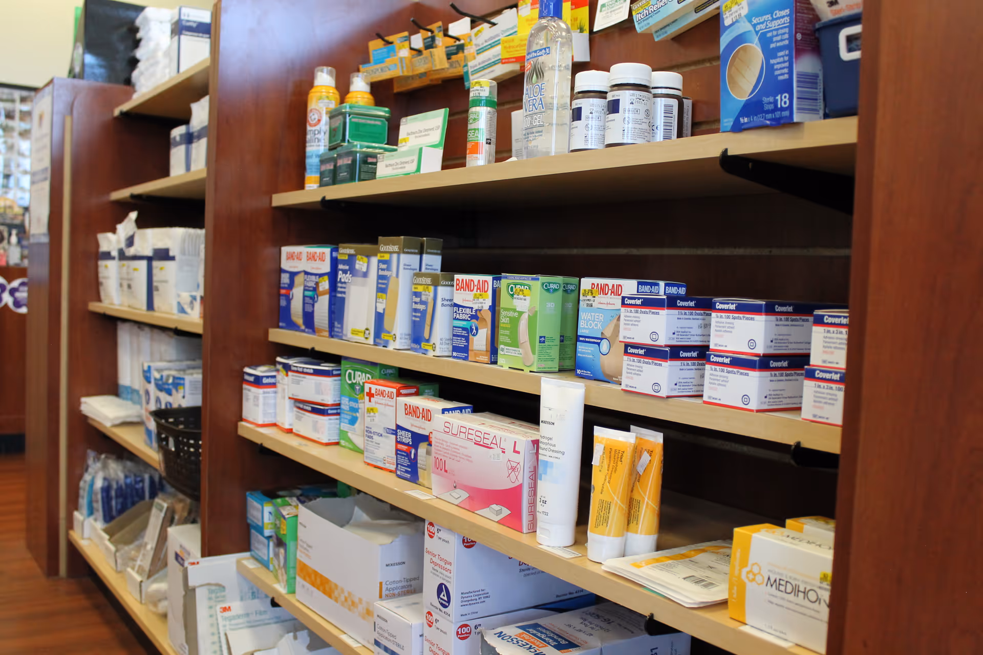 Wooden shelves stocked with medications and medical supplies in a facility storage area.