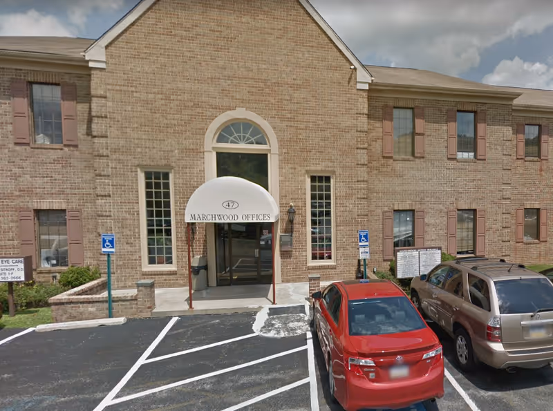 Brick building with arched entrance, glass doors, and parked cars in front.