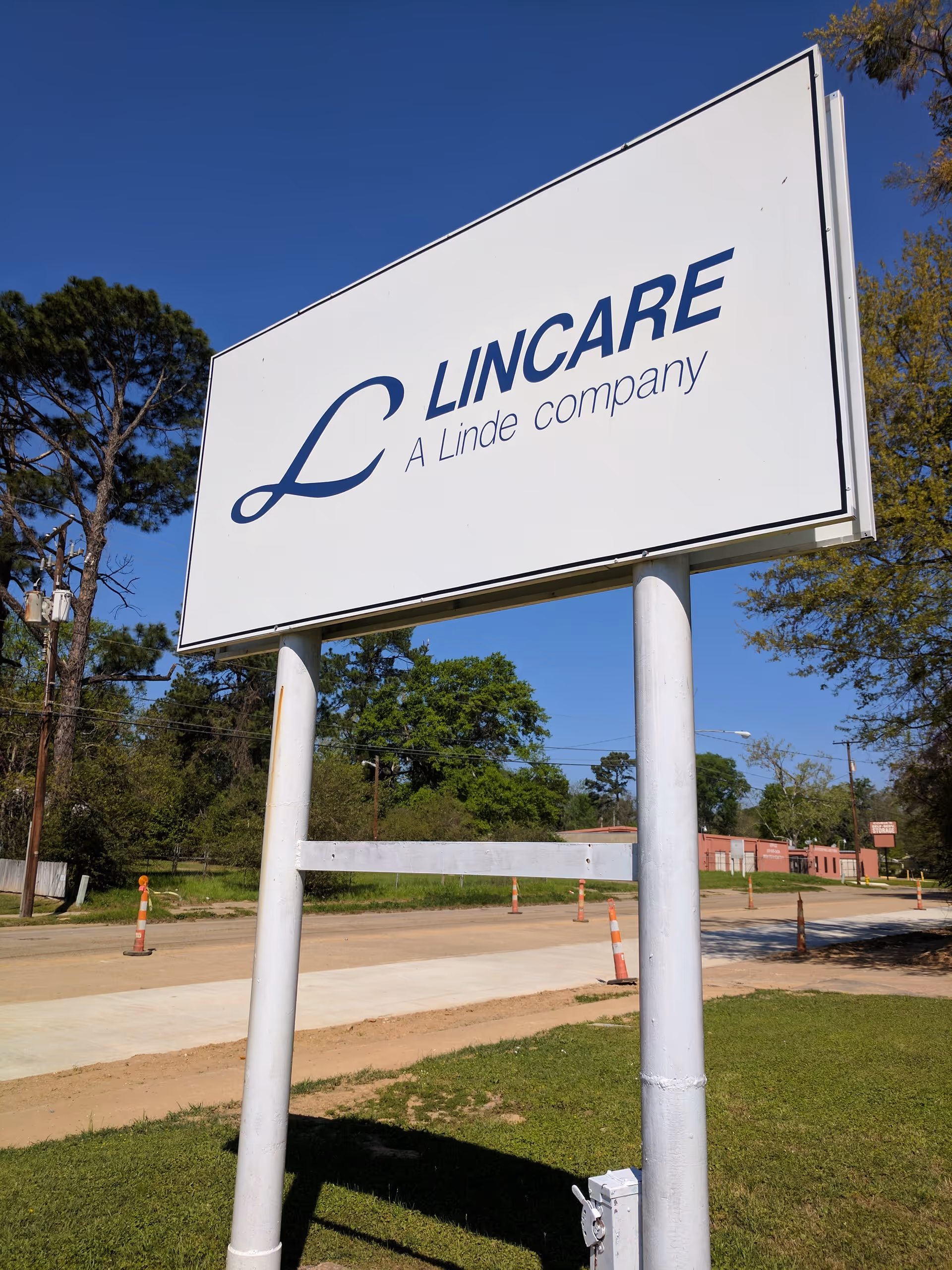A large LINCARE sign on two white posts stands outdoors with trees and blue sky.