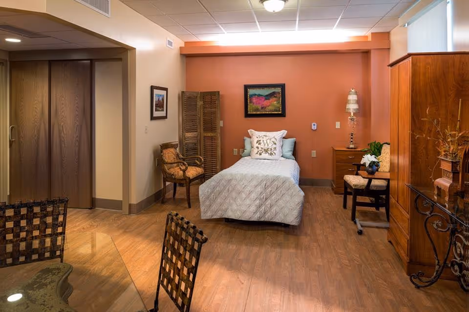 A cozy hospice bedroom with a central bed, chairs, and wooden furniture against coral walls.