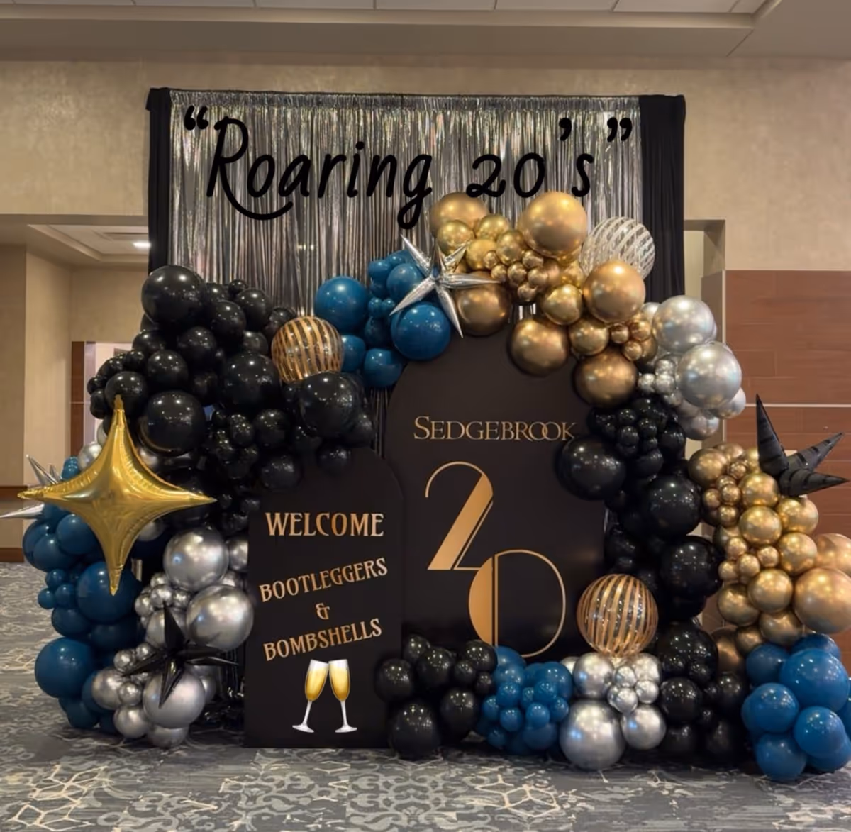 Indoor event setup with a balloon arch and Roaring 20s backdrop.