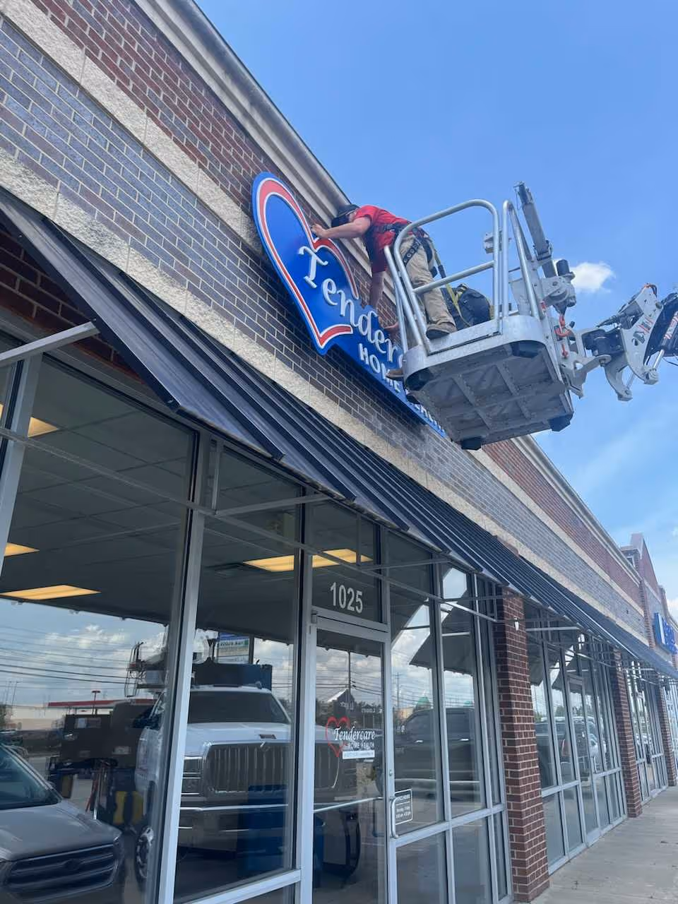 A worker on a lift installs a sign on the exterior of a brick building.