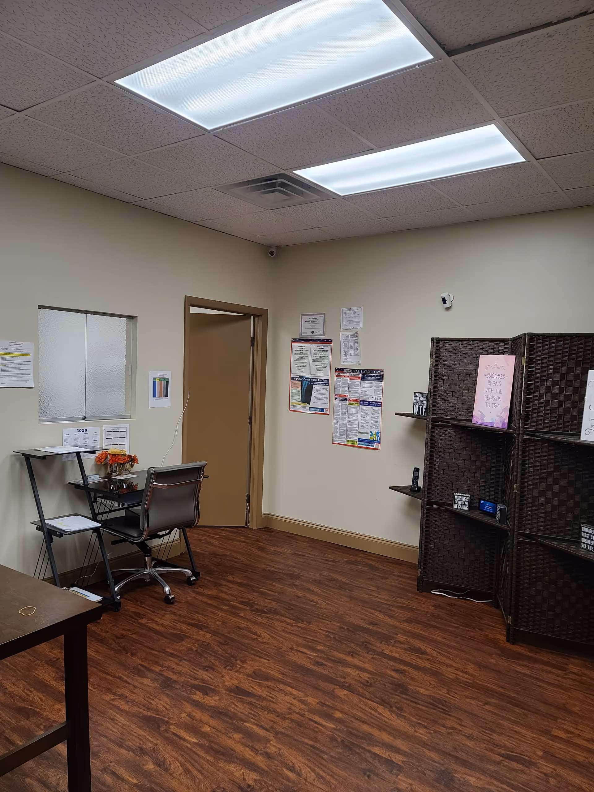 Interior office and reception area with desk, chair, shelves, and notices.