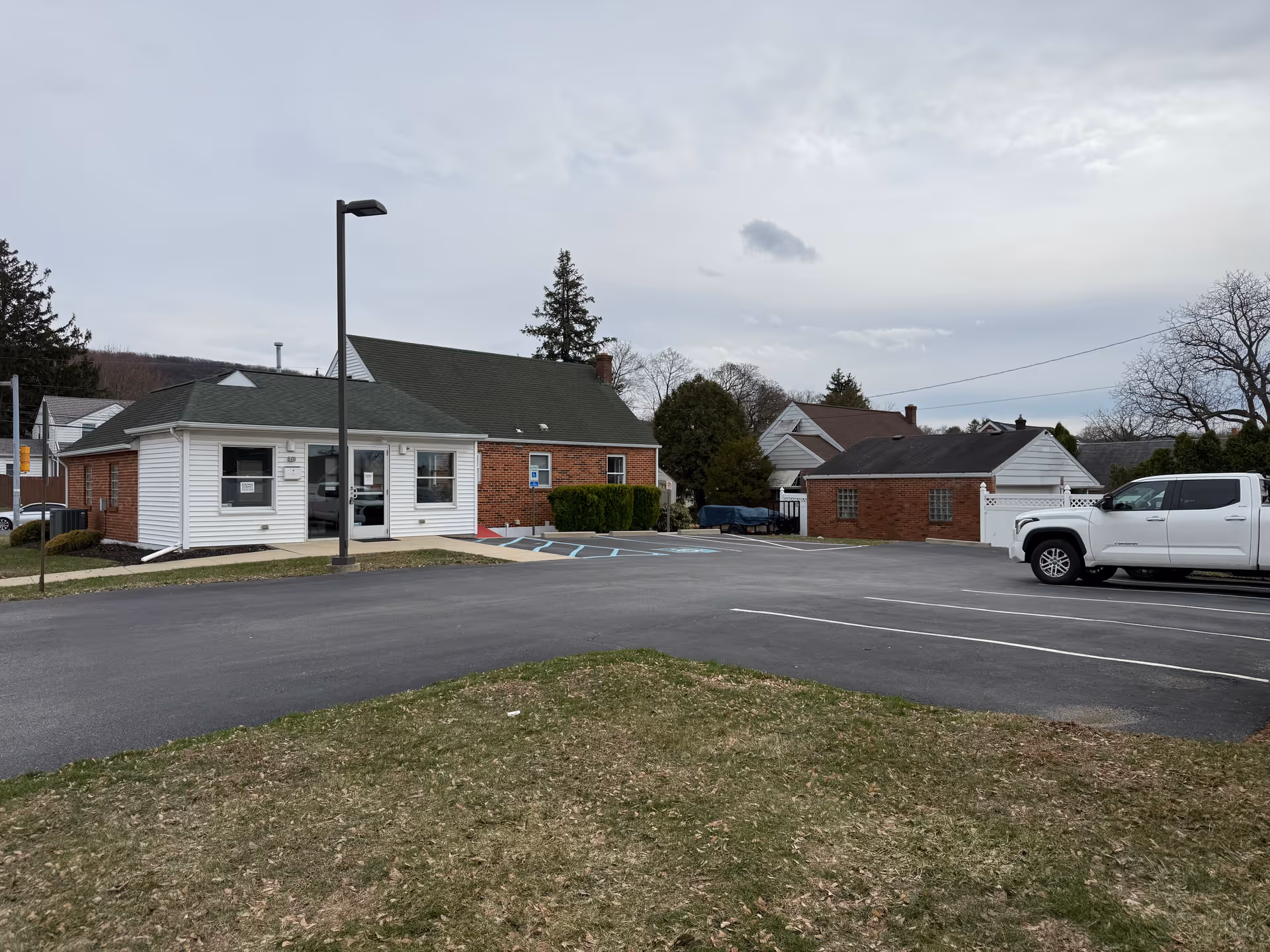 A single-story brick and white siding building with a paved parking lot and a white truck.