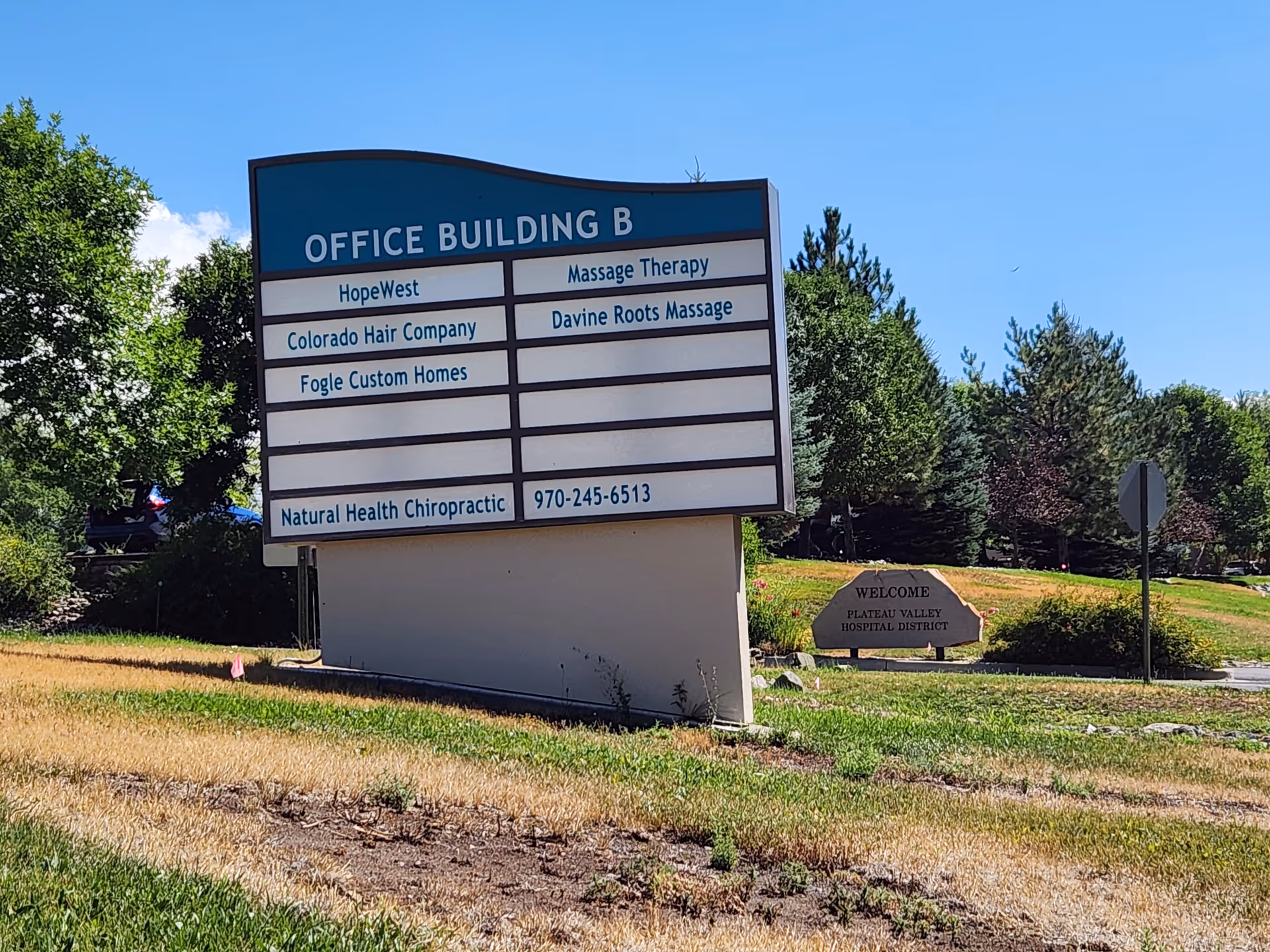 Exterior sign for HopeWest Administrative Offices reading OFFICE BUILDING B, with surrounding trees and blue sky.